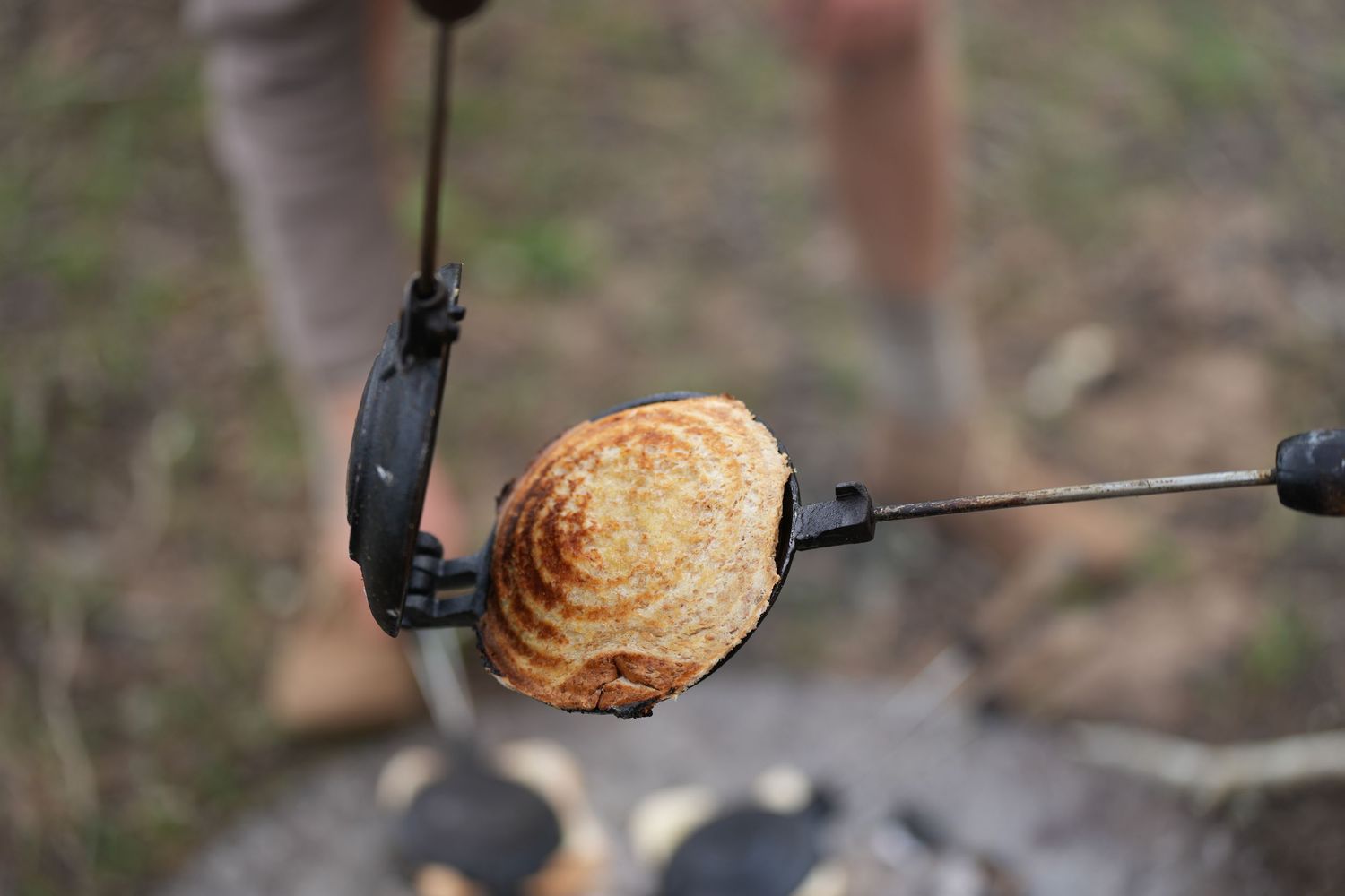 Close-up of a golden brown toast being cooked on an outdoor camping toaster.