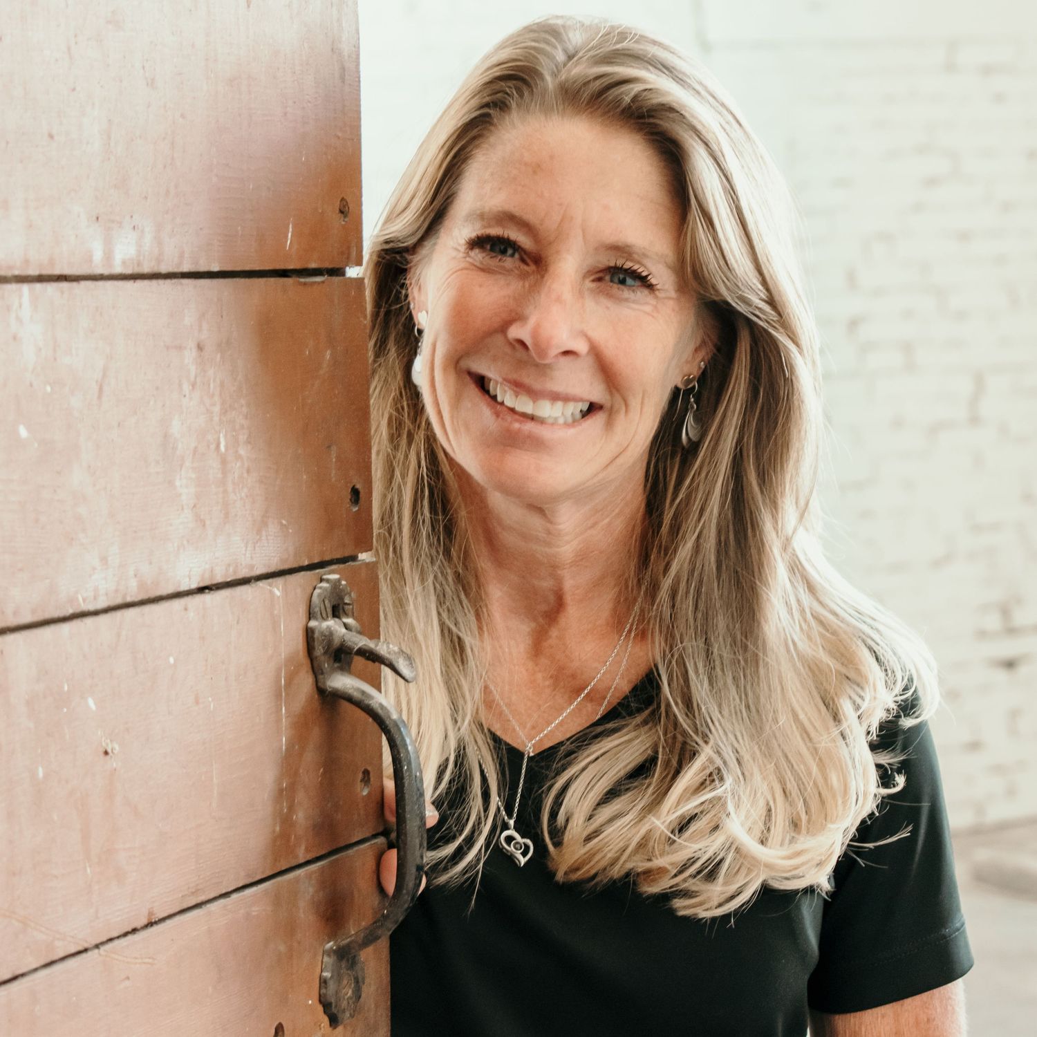 A casual outdoor portrait showing warm smile and blonde hair against a textured wall.