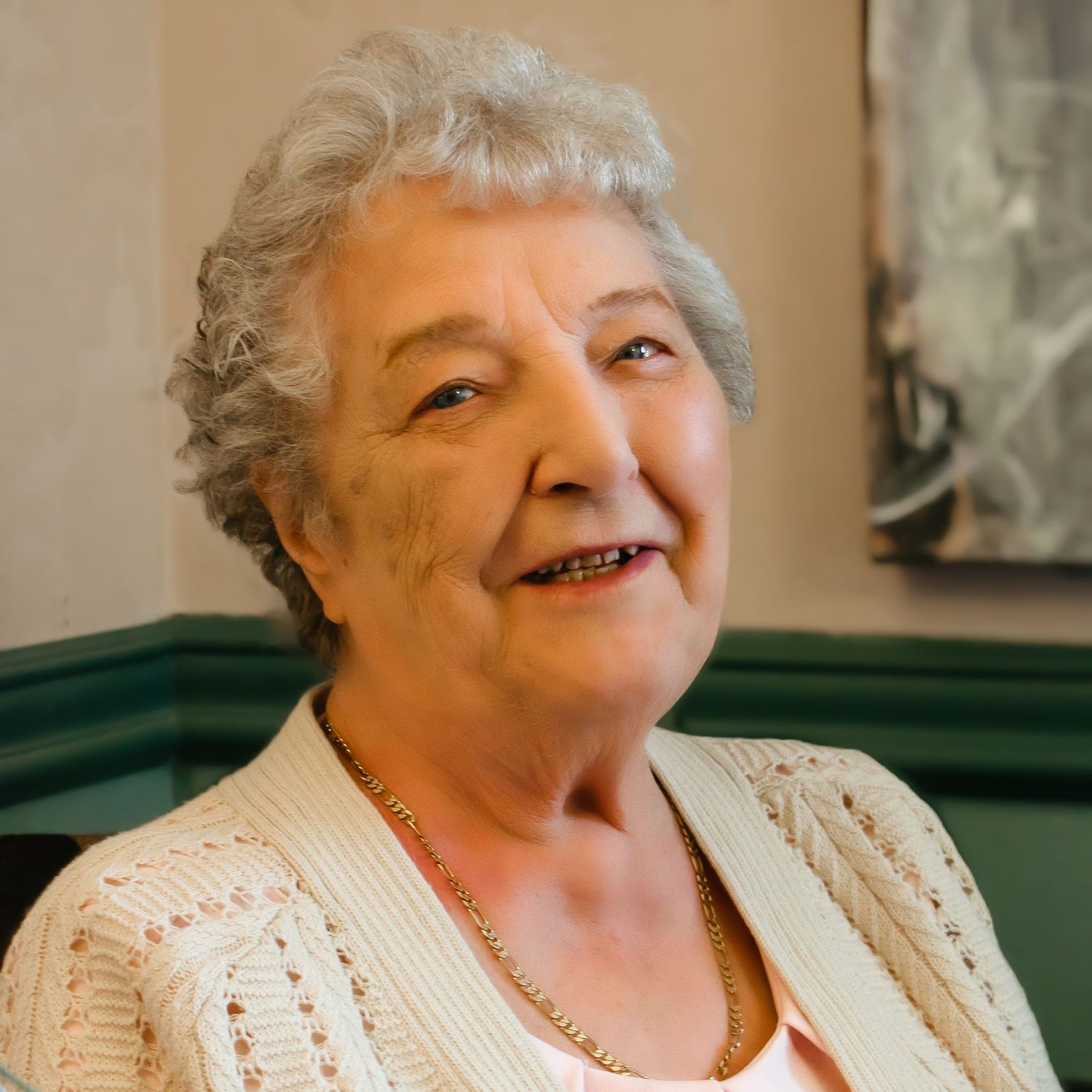 Smiling senior wearing a cream knitted sweater and pearl necklace in a warm indoor setting.