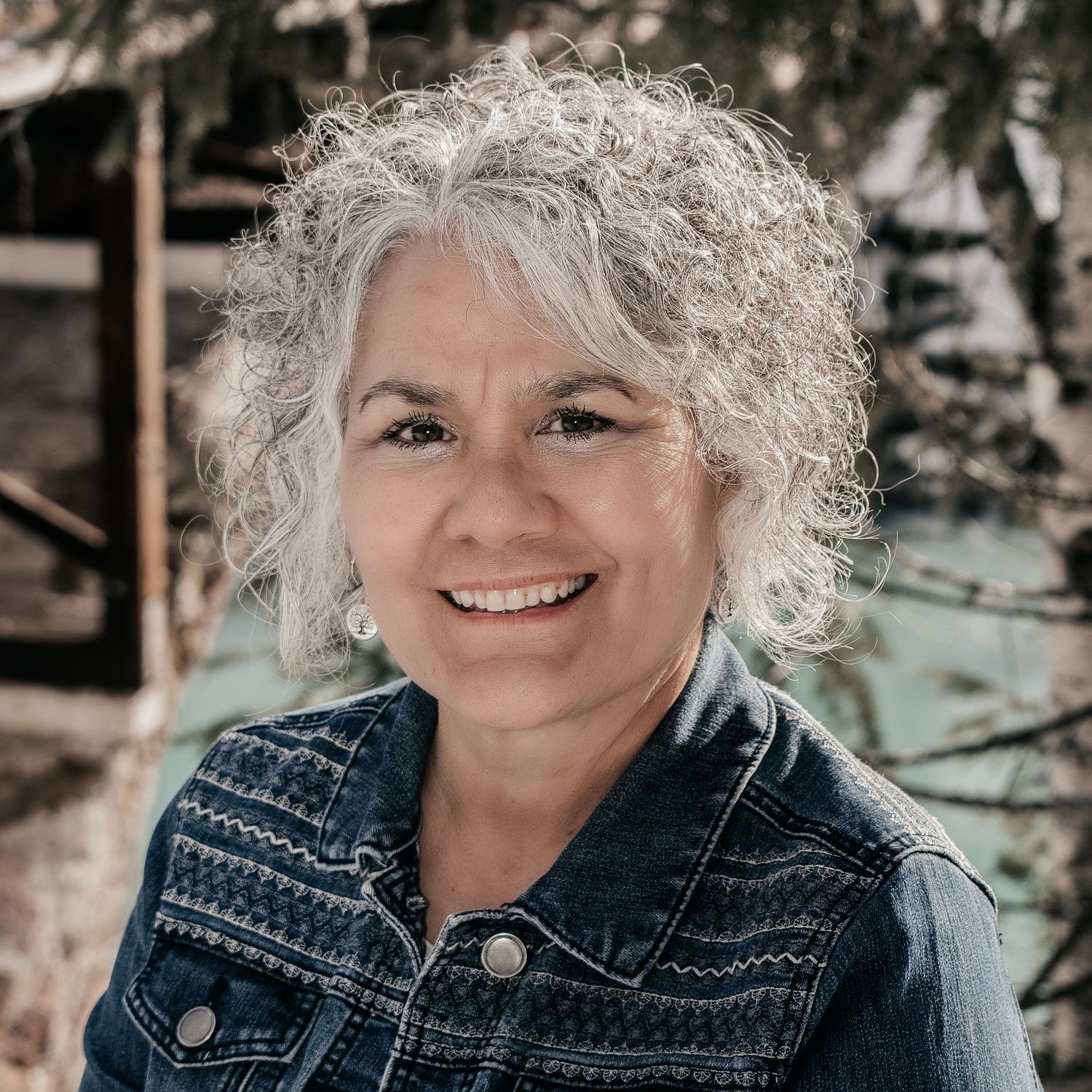 Candid portrait of woman with natural gray curly hair wearing denim jacket outdoors.