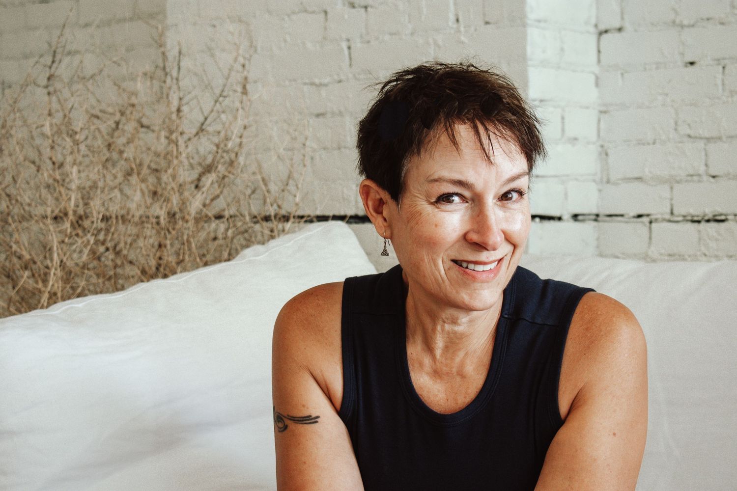Athletic woman in black tank top smiling against white backdrop.