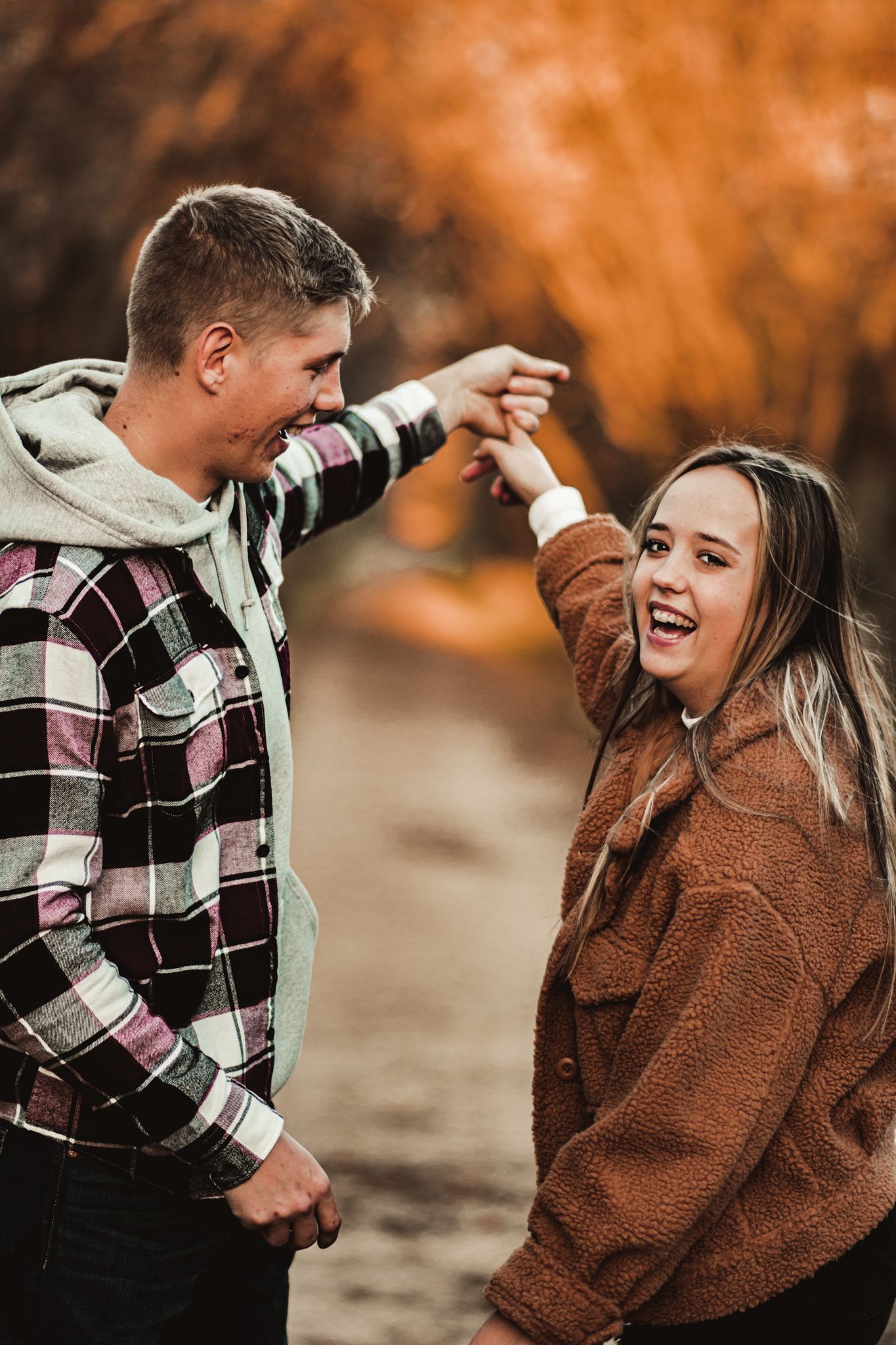 Joyful couple dancing and laughing together on autumn path with orange foliage.