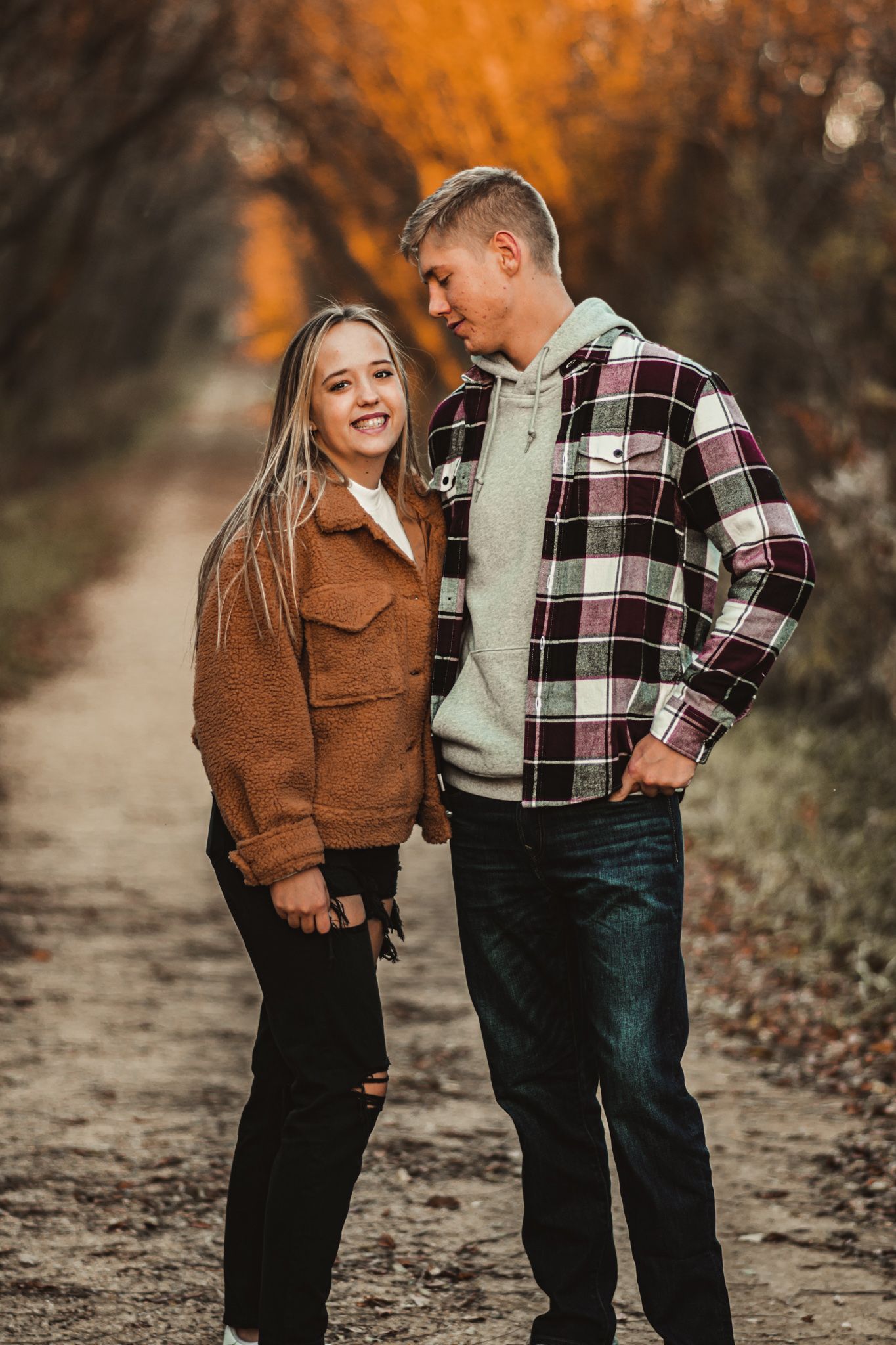 Happy couple in casual fall outfits sharing moment on leaf-lined autumn trail.