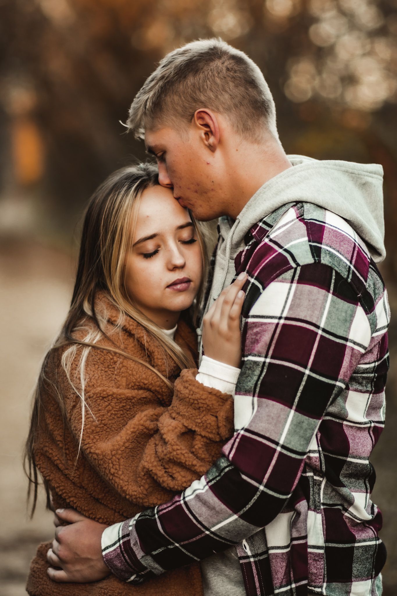 A tender moment between a couple wearing plaid and brown cozy sweaters against an autumn backdrop.