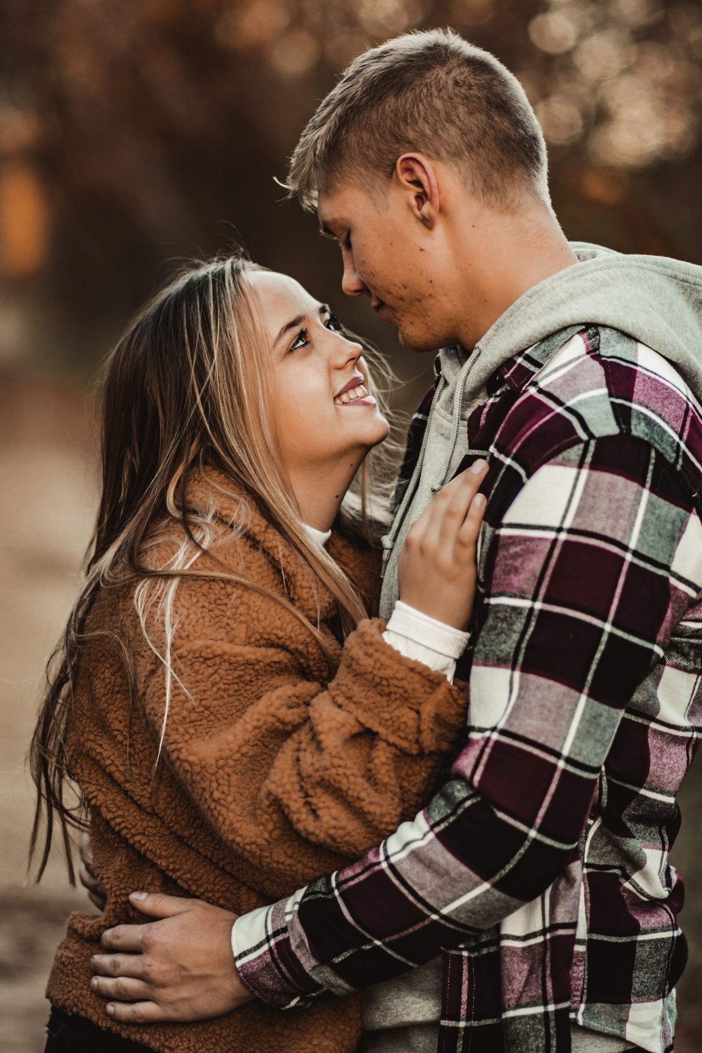 Couple in plaid and brown cozy sweaters sharing intimate moment on autumn trail.