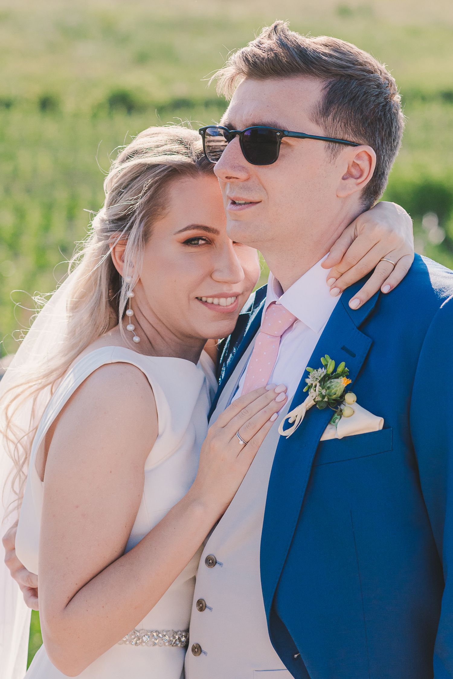 Couple in blue suit and white dress sharing intimate moment in sunlit field.