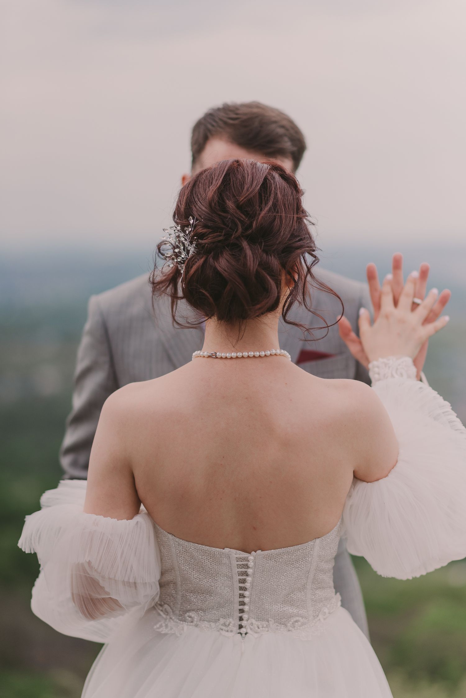Back view of a bride in a white corset dress against a misty landscape.