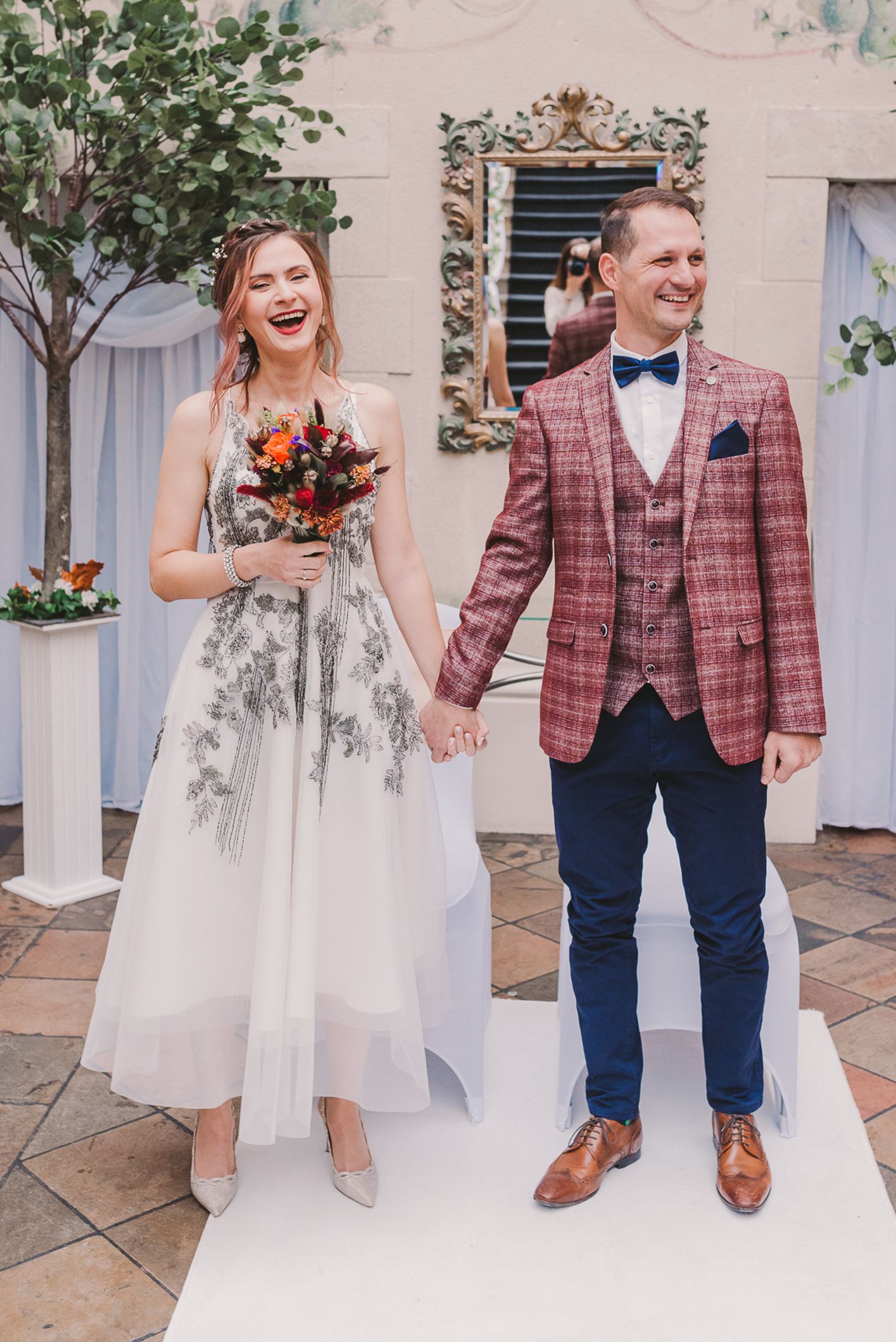 Wedding couple in white dress and plaid jacket posing on stone patio.