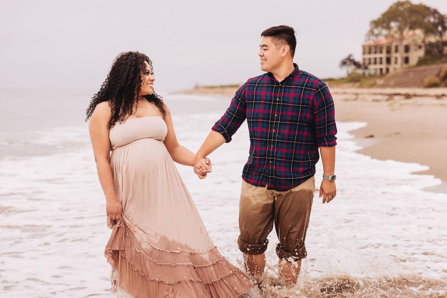 Couple holding hands on beach wearing coordinated outfits with waves lapping at their feet.
