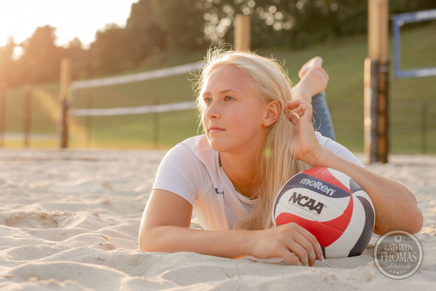 Athlete resting on sandy court with volleyball during golden hour photoshoot.