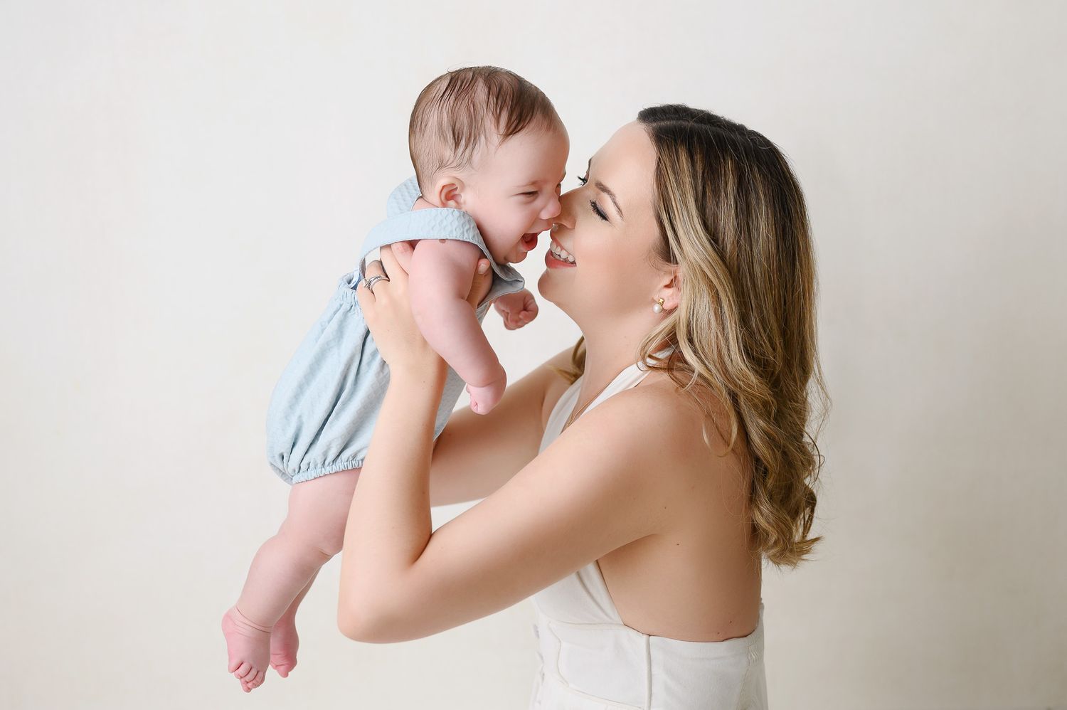 Mother and baby sharing joyful intimate moment against white backdrop.