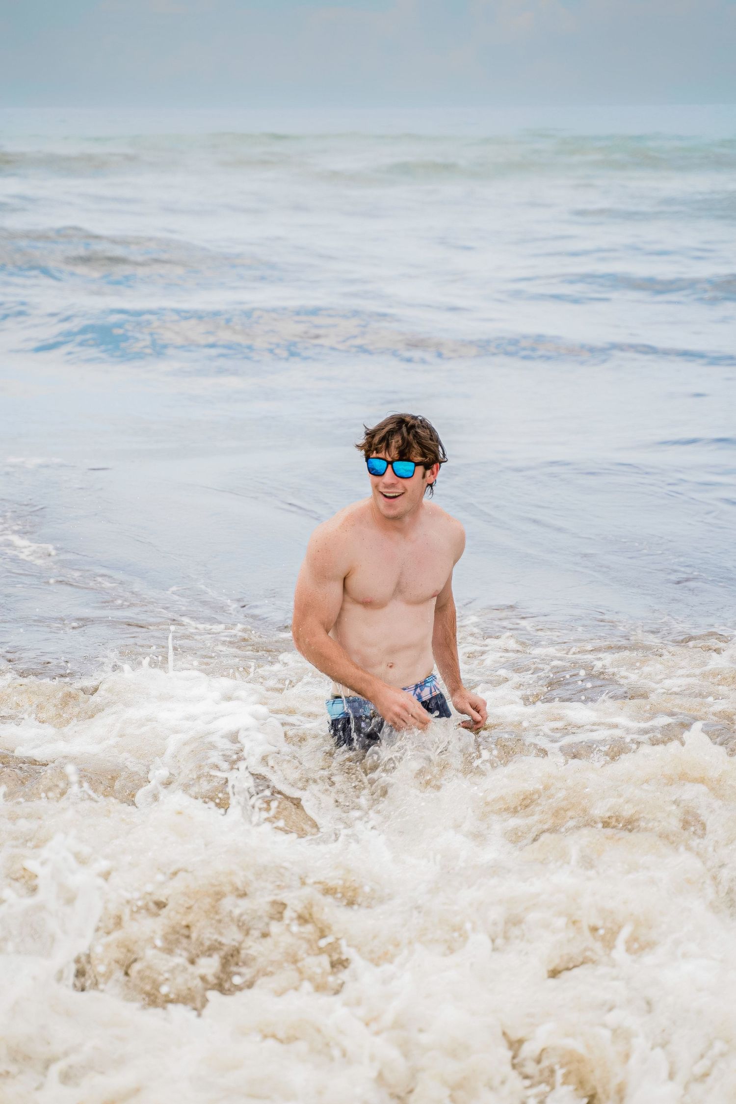 A swimmer in blue goggles enjoys splashing through the rough surf at the beach on a cloudy day.