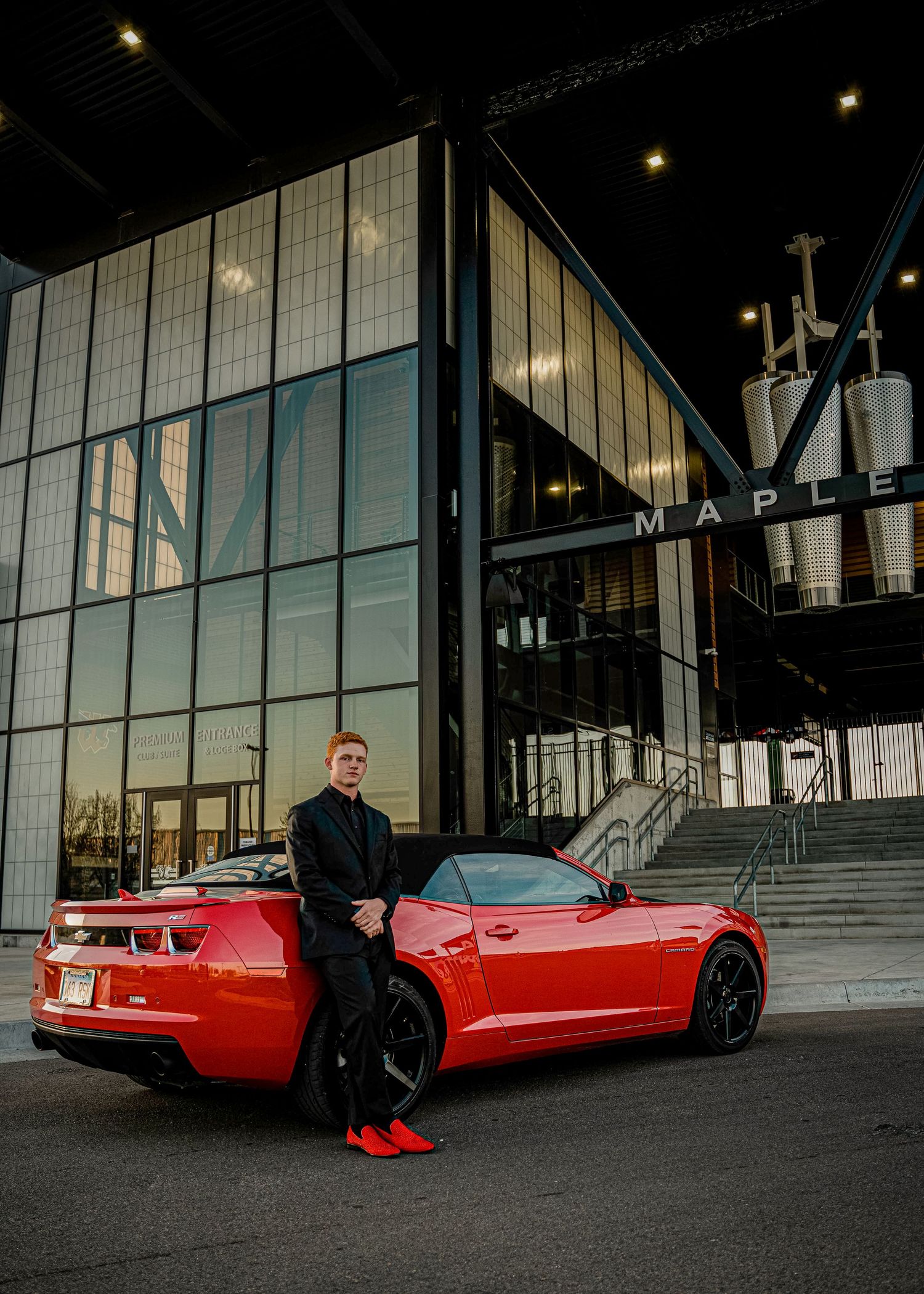 Modern glass building facade with red sports car parked outside at dusk with illuminated lighting.