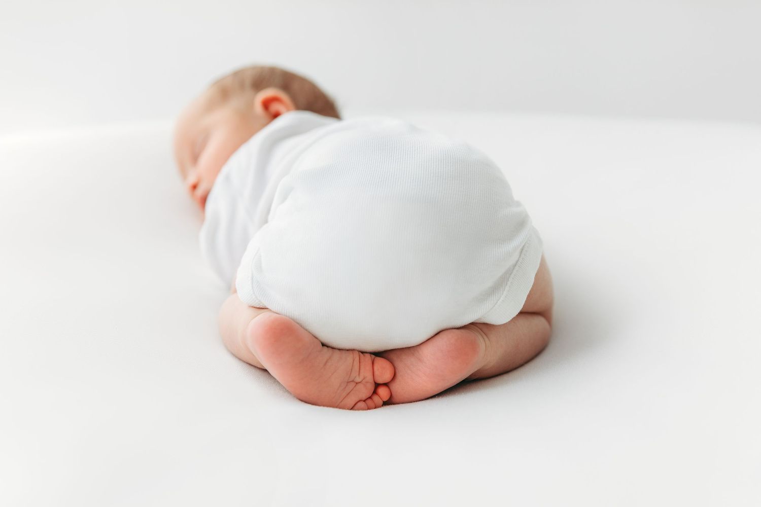 Close-up view of tiny feet tucked under a curled-up sleeping baby