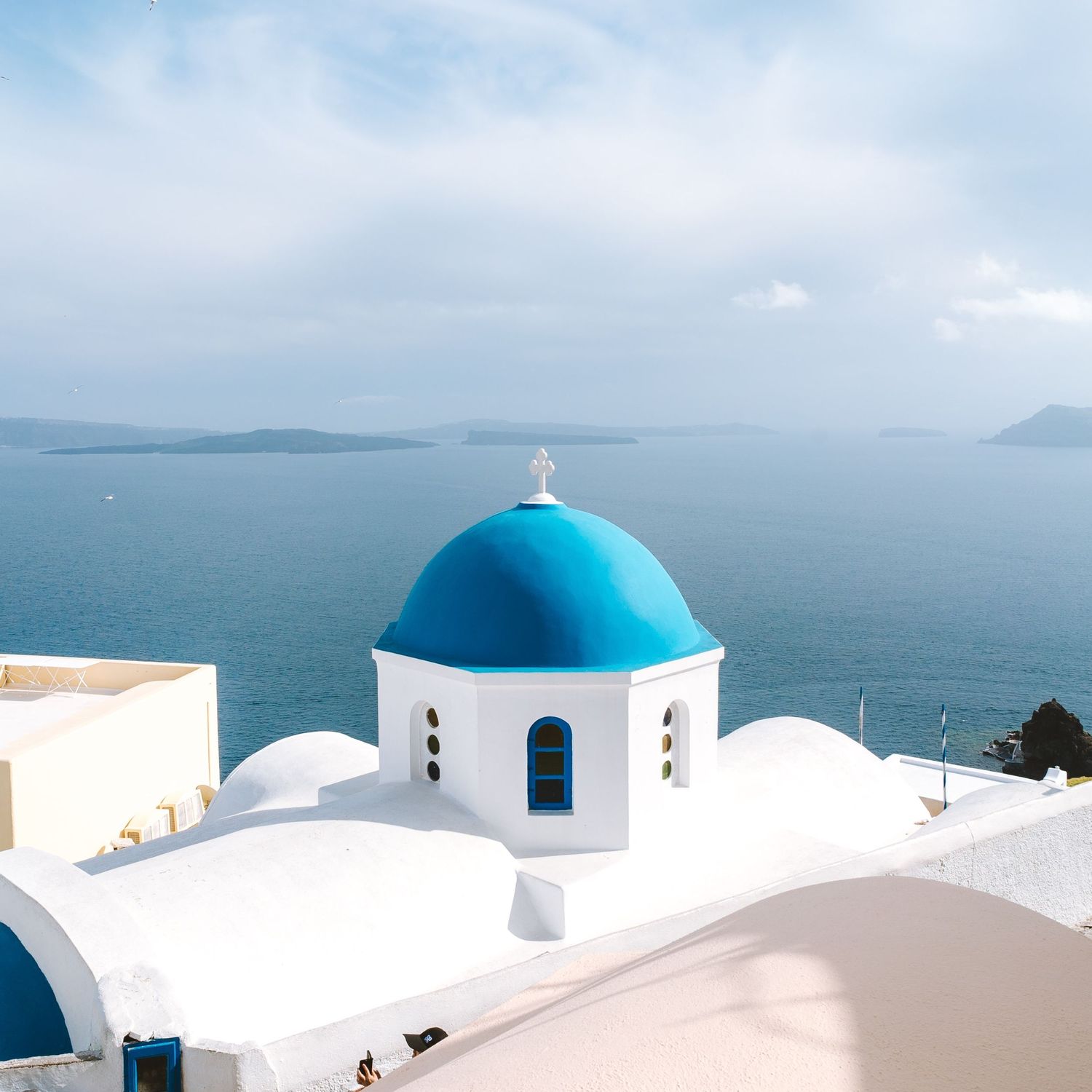 Sunrise on the Infamous blue dome of a white church in Santorini, Greece. Church stands in front of vast ocean waters.