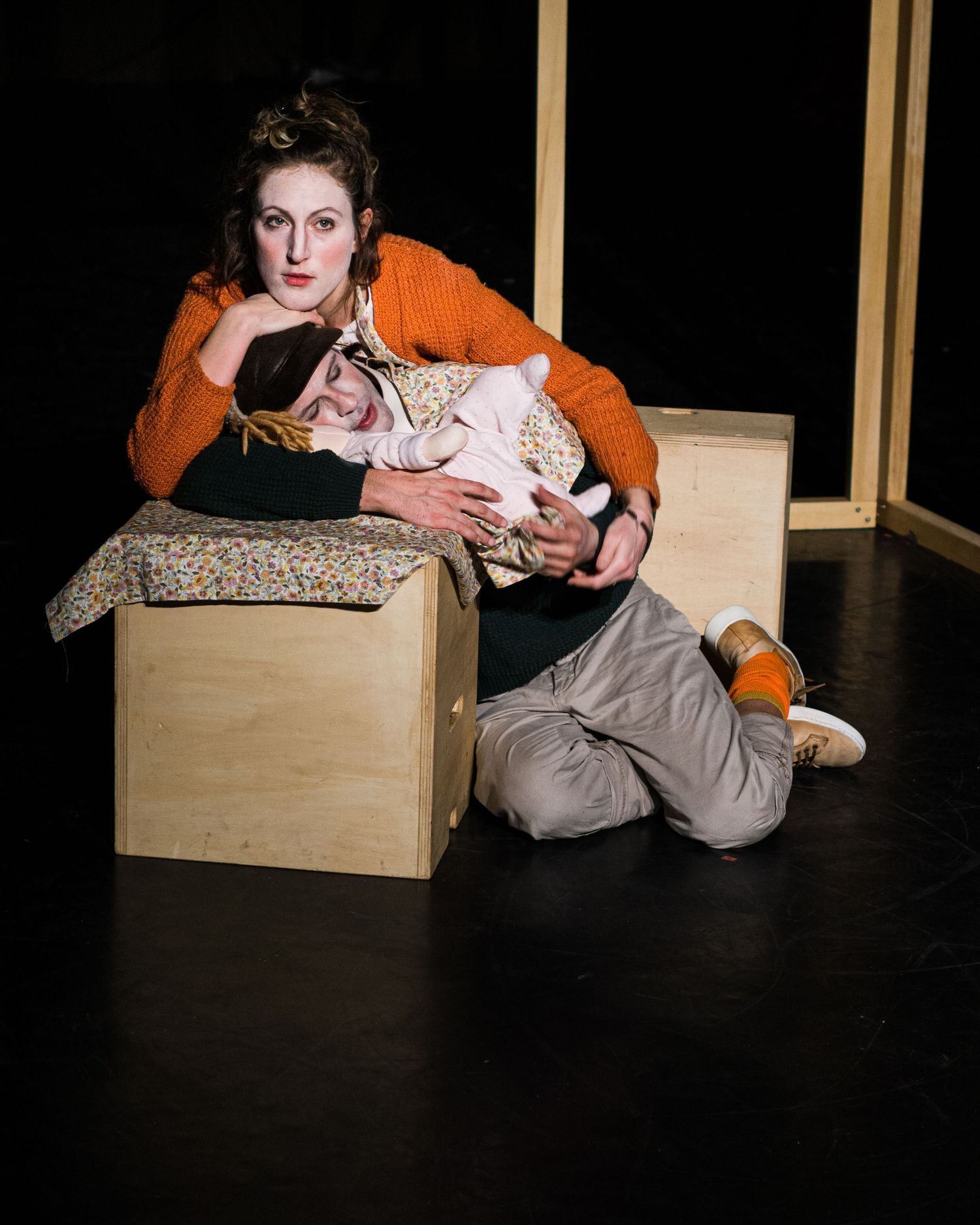 A theatrical scene showing performers resting on a wooden box during a dramatic moment.