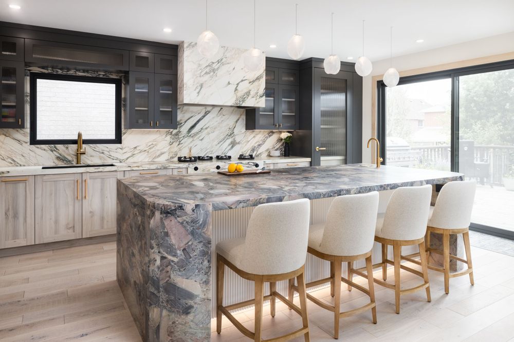 Modern luxury kitchen with marble backsplash, light wood cabinets, and white bar stools at a curved island.