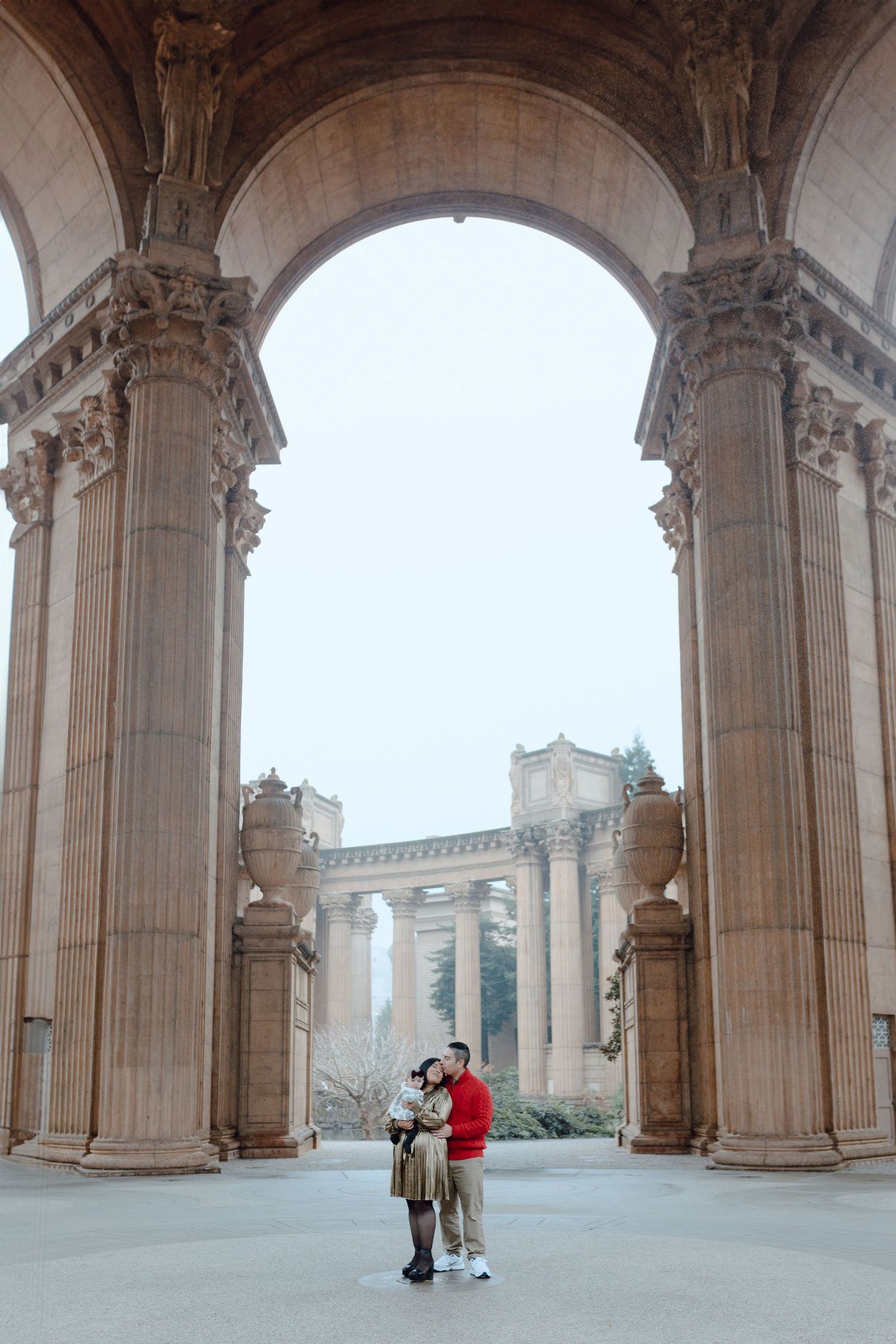 Romantic couple embracing under ornate stone archway at Palace of Fine Arts.