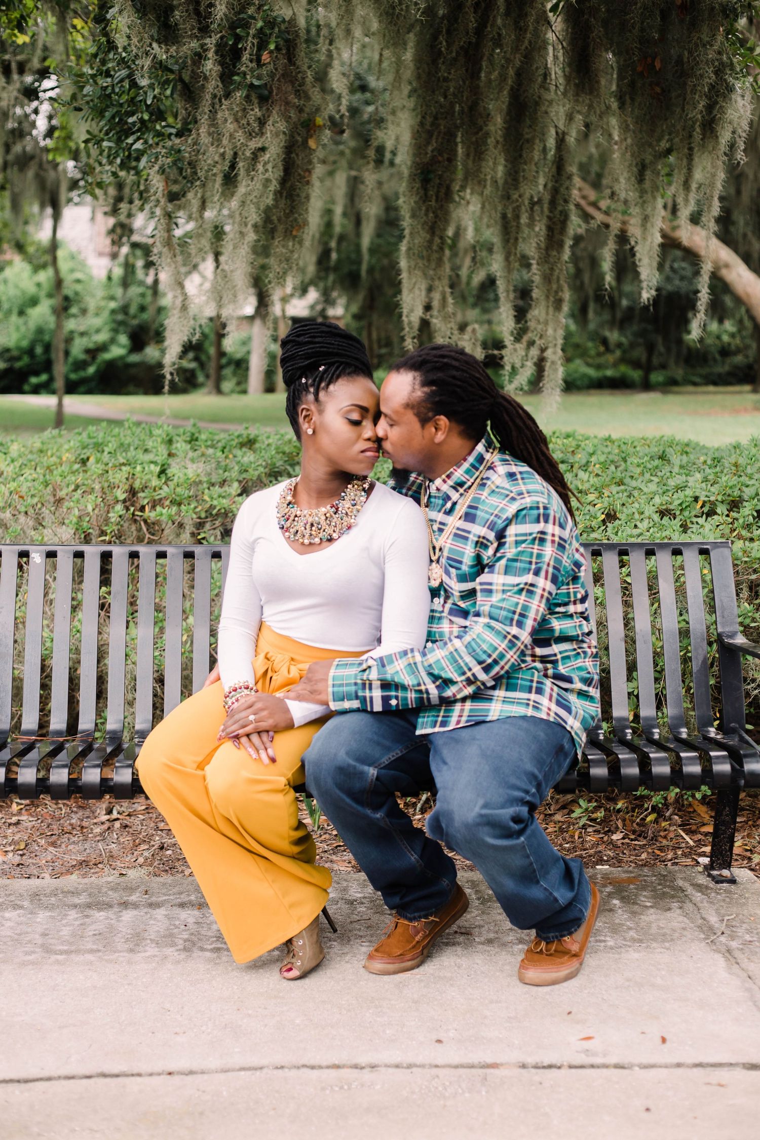 A romantic couple shares an intimate moment on a park bench under Spanish moss trees.