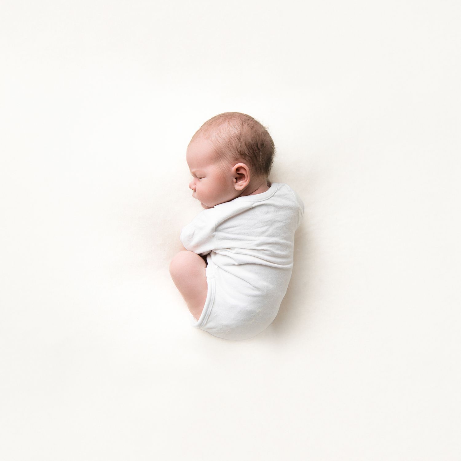 A sleeping newborn wrapped in white fabric lies peacefully against a white background.