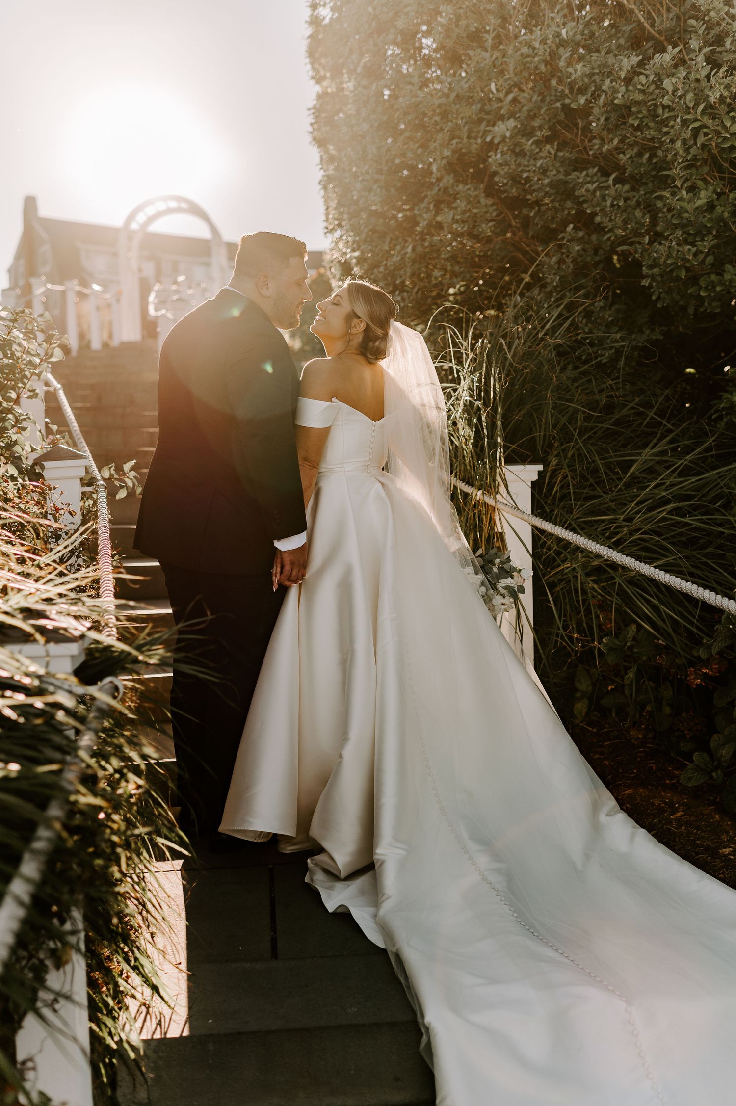 Golden sunlight illuminates wedding couple walking along garden pathway.
