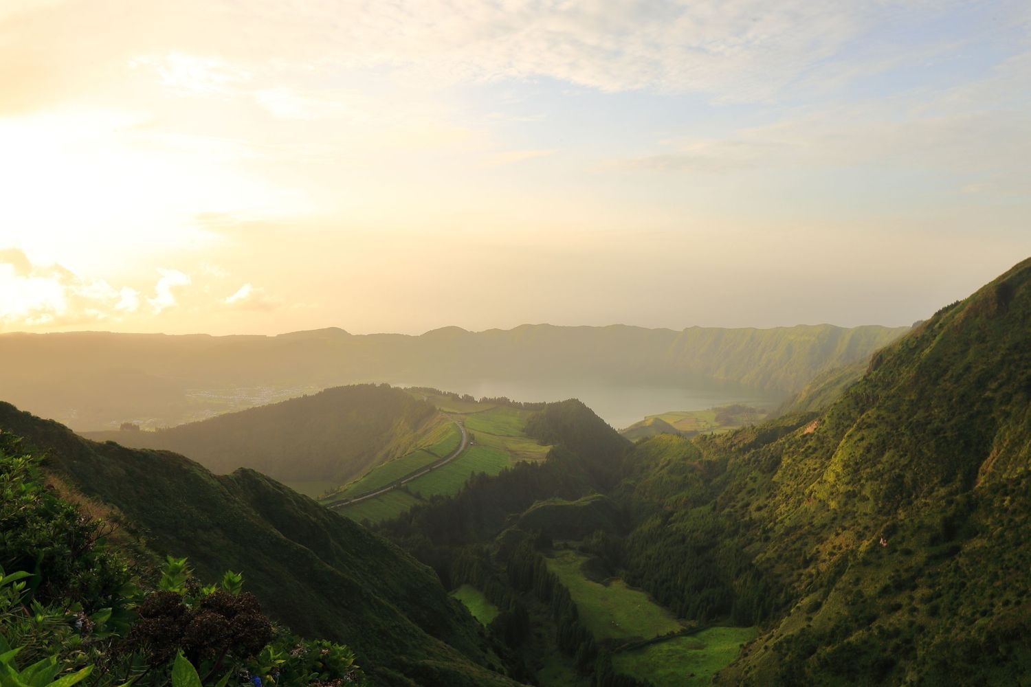 Verdant mountain valley landscape bathed in warm sunset light with rolling hills.
