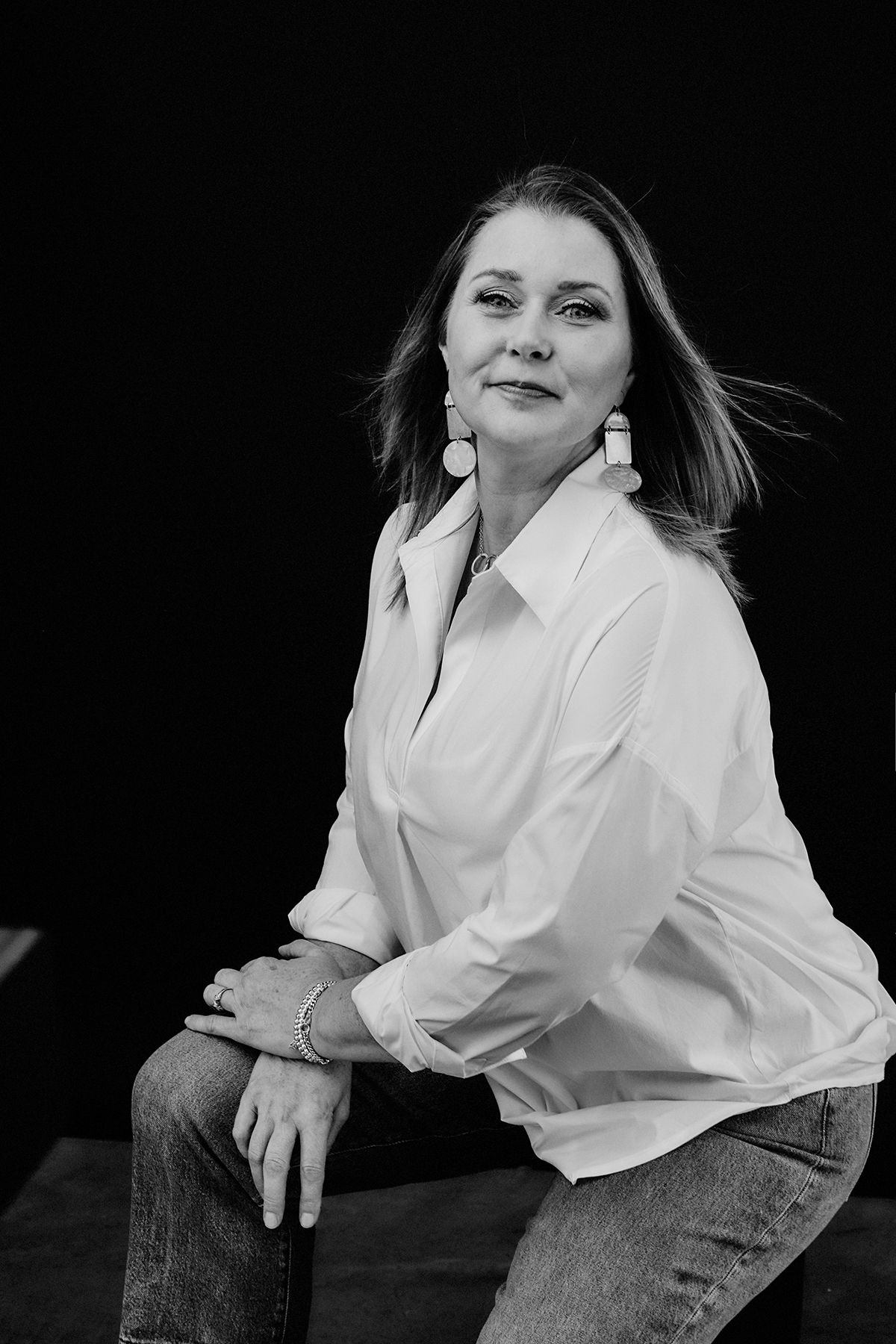 Dramatic black and white portraits in white shirt and jeans against dark background.