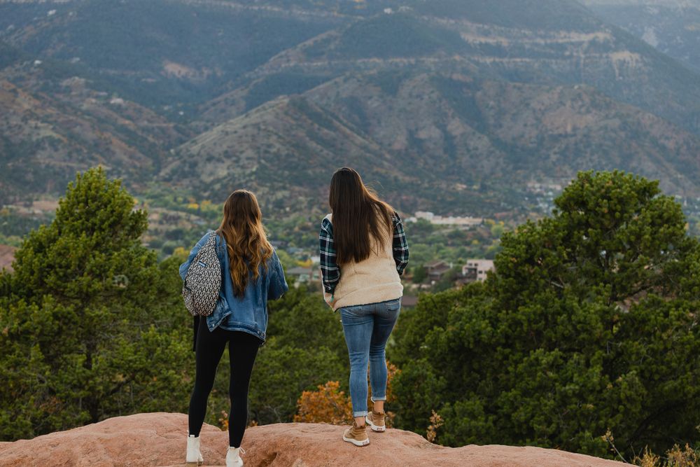 Two hikers enjoy mountain views while standing on a rocky overlook.