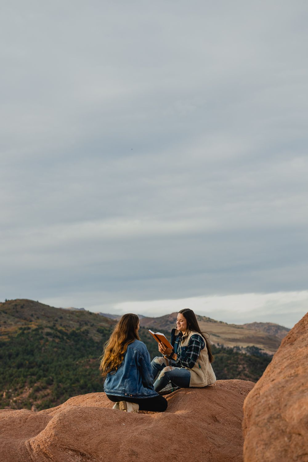 Friends having an intimate conversation while perched on red rocks with mountains in the background.