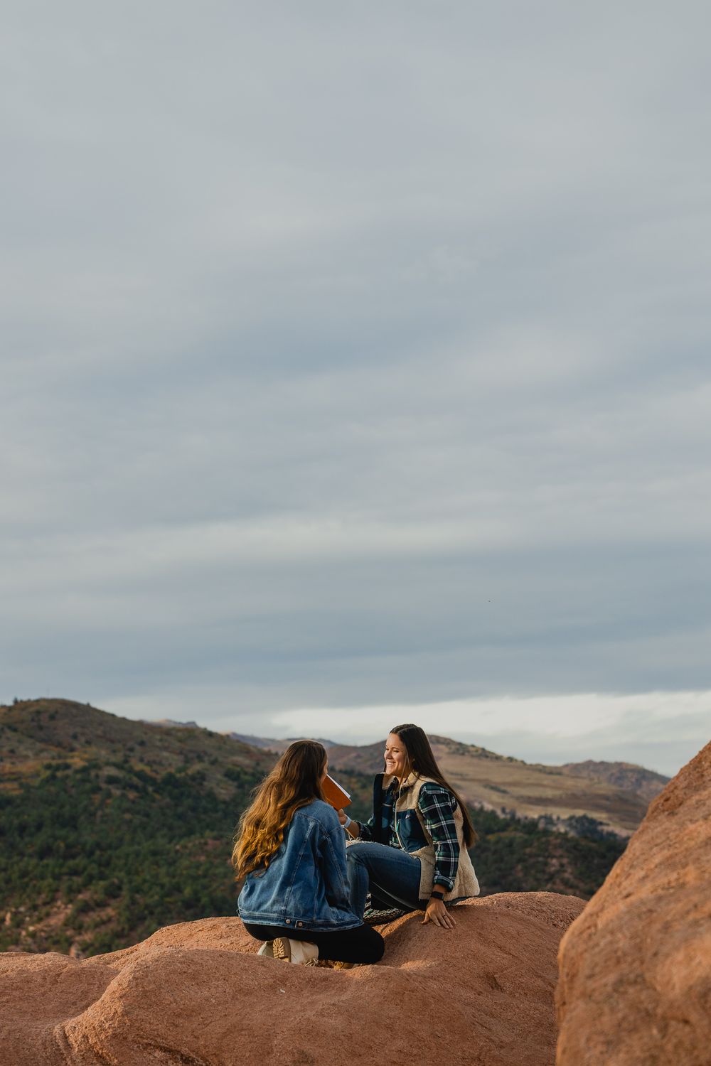 Two people sharing a conversation while sitting on red rocks with scenic mountain views.