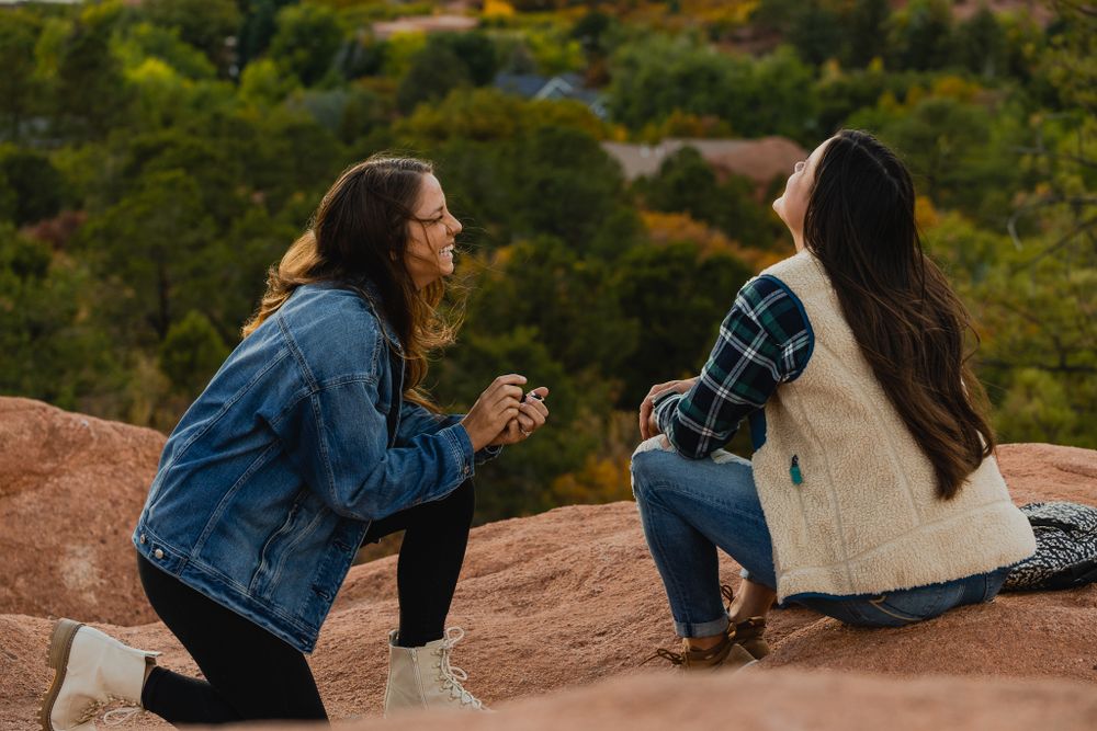 A romantic proposal taking place on red rocks overlooking a scenic mountain landscape.