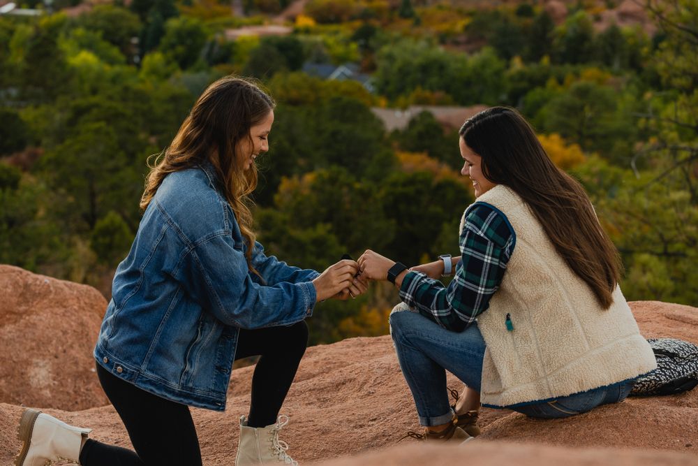 A couple sharing an intimate proposal moment on red rocks with mountains in the background.