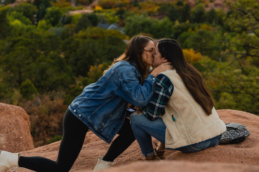 Two people sharing their first kiss after a proposal on scenic red rocks.