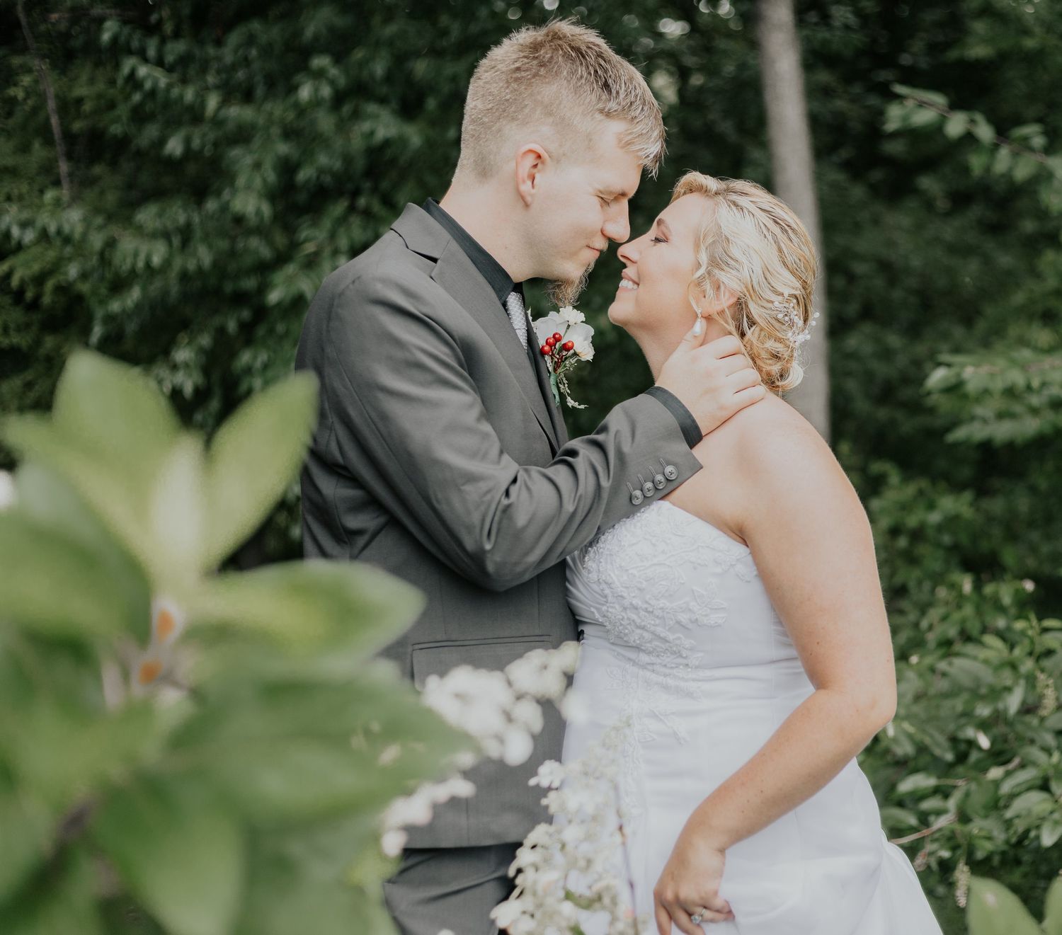 Intimate moment between newlyweds in formal wedding attire among green foliage.
