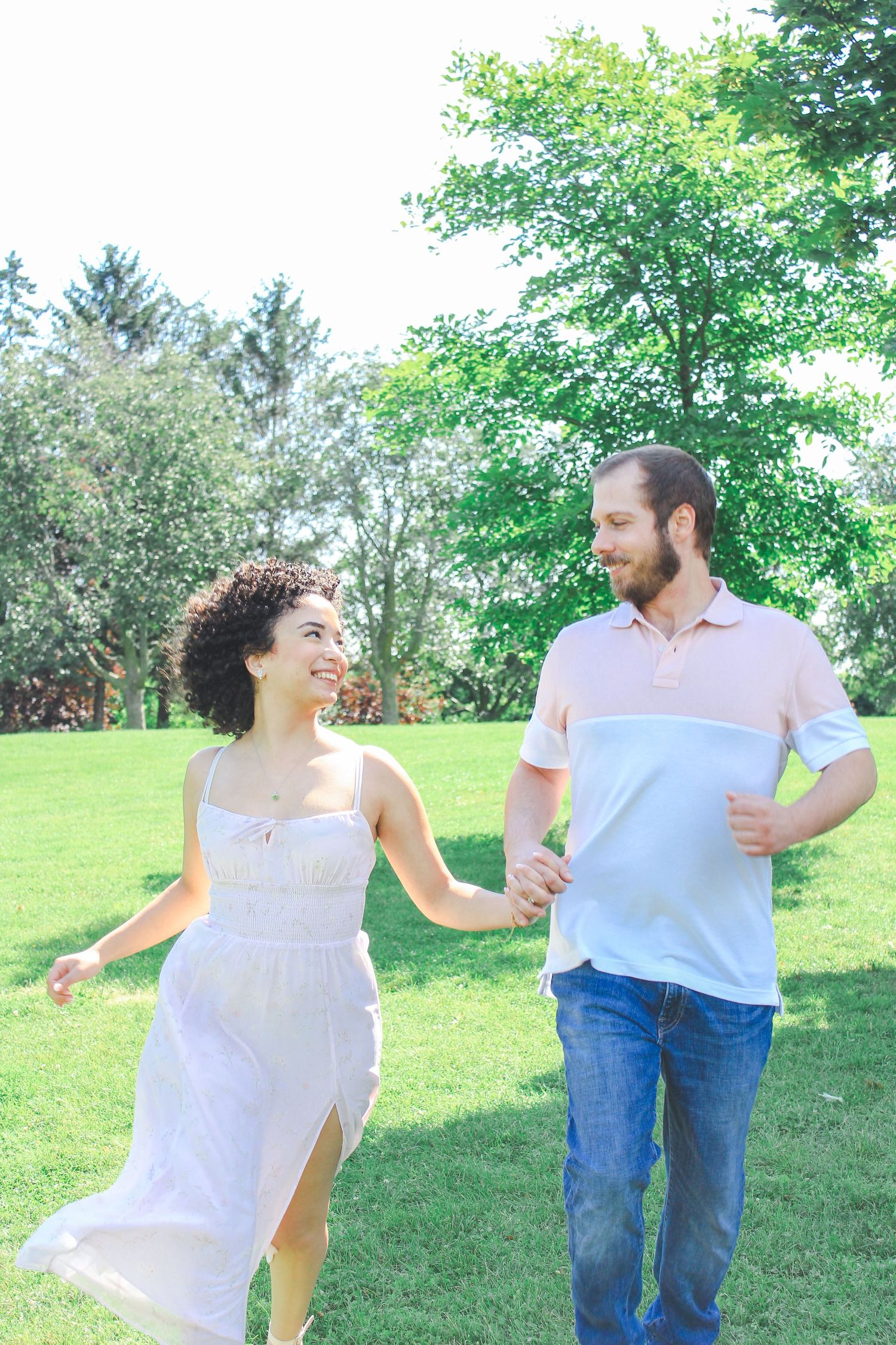 A couple strolls hand in hand through a lush green park on a sunny summer day.