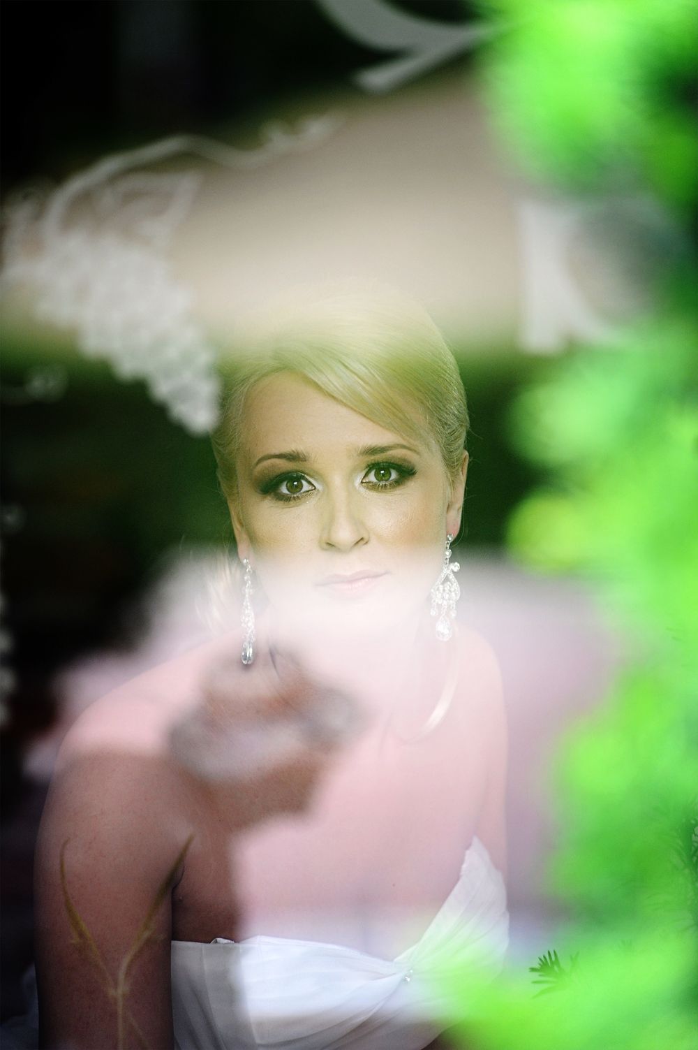 A soft focus bridal portrait with ethereal lighting and green foliage accents.