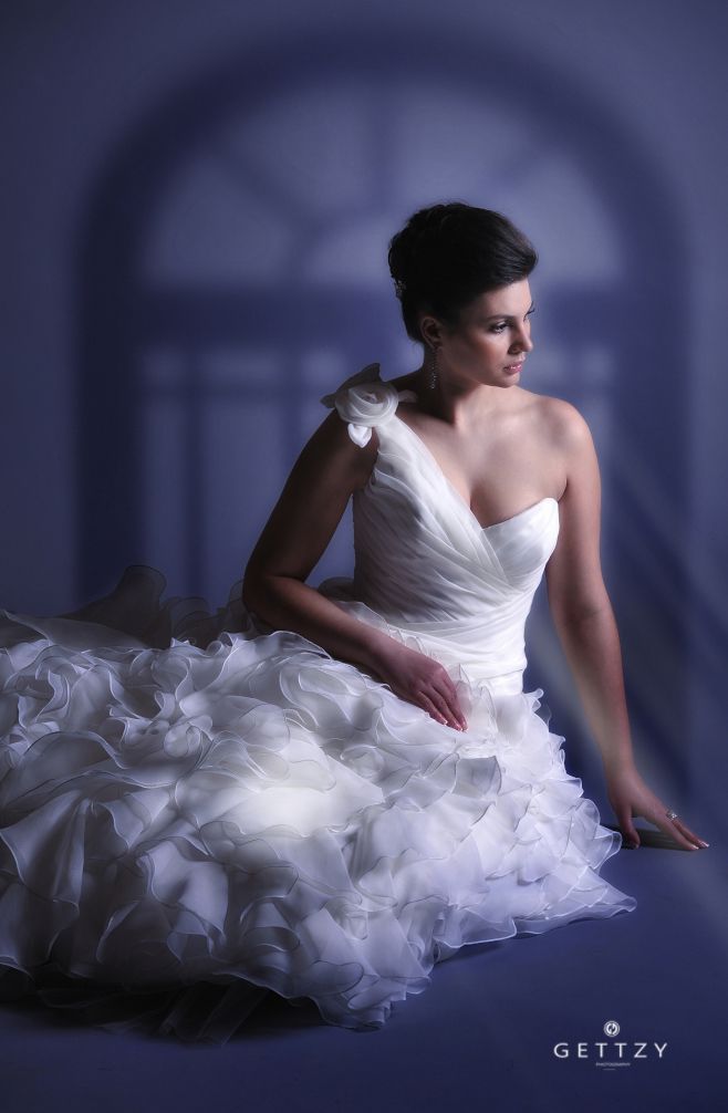 An artistic bridal portrait in purple lighting featuring a ruffled wedding dress and dramatic pose.