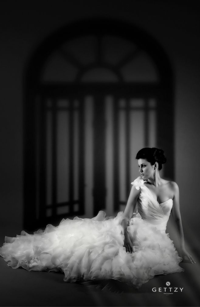 A dramatic black and white bridal portrait featuring a flowing wedding gown against an arched backdrop.