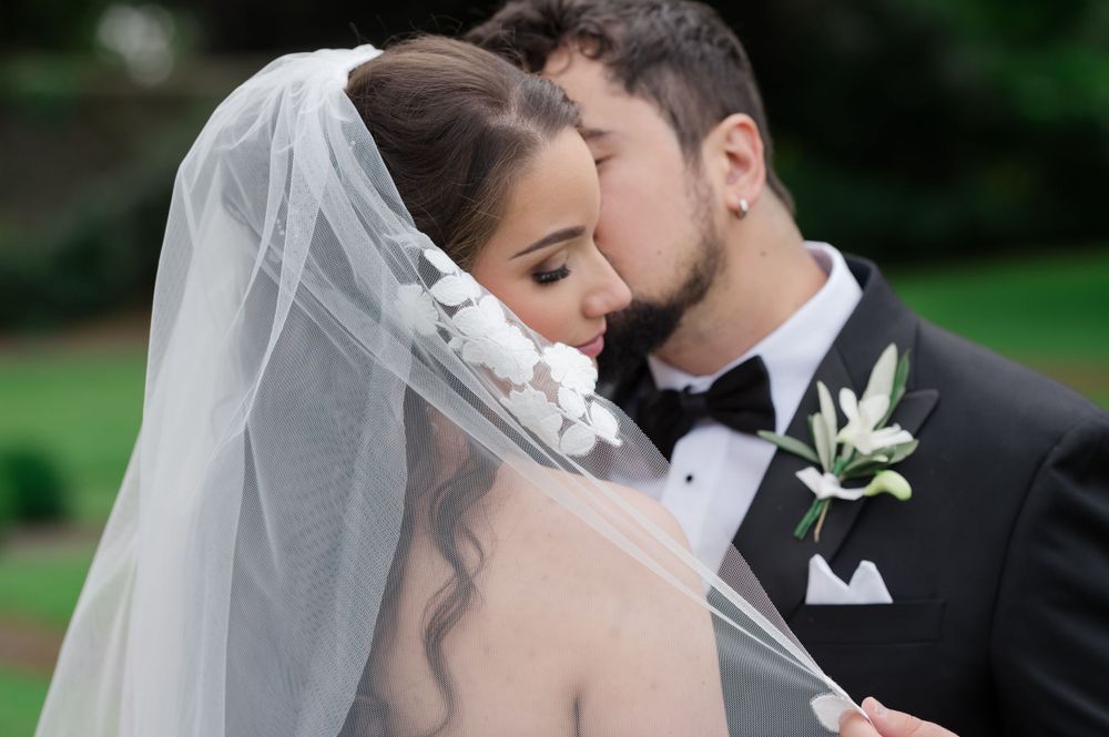 A groom in a black tuxedo kisses his bride wearing a white veil on their wedding day outdoors at Tankardstown House Co.Meath