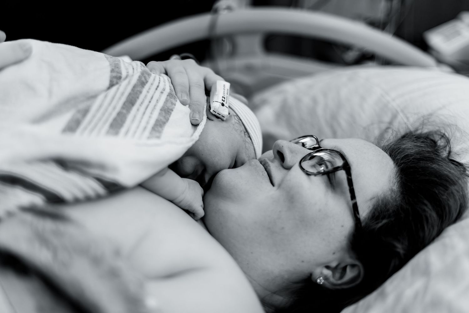 An intimate black and white portrait showing a tender moment between parent and newborn in hospital.