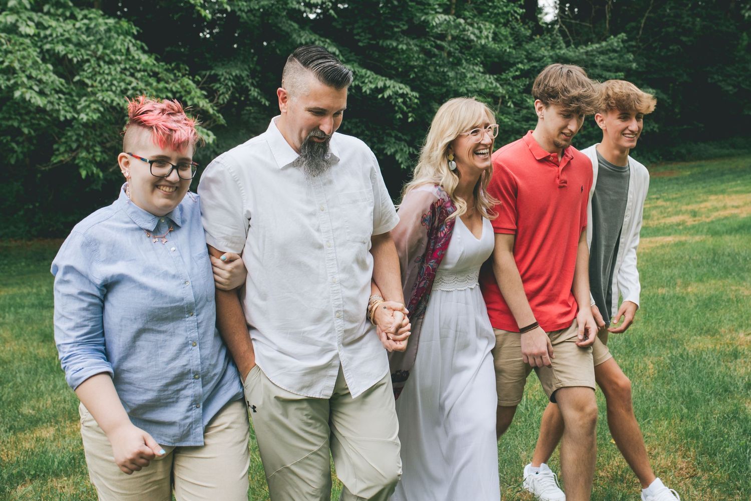 Group walking together on grass with trees in background wearing casual summer attire.