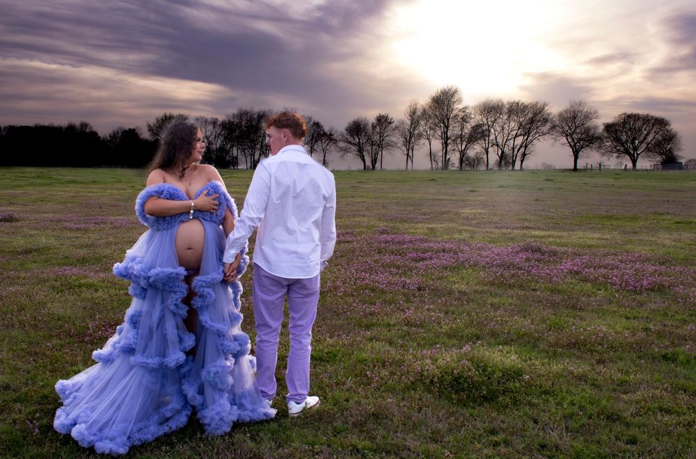 Couple in blue and white formal attire poses in a rustic field at sunset for romantic portraits.