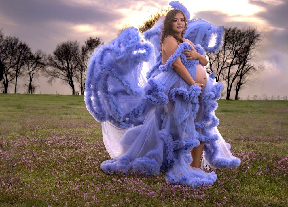 Dramatic outdoor portrait session with flowing periwinkle dress against a moody sunset sky.