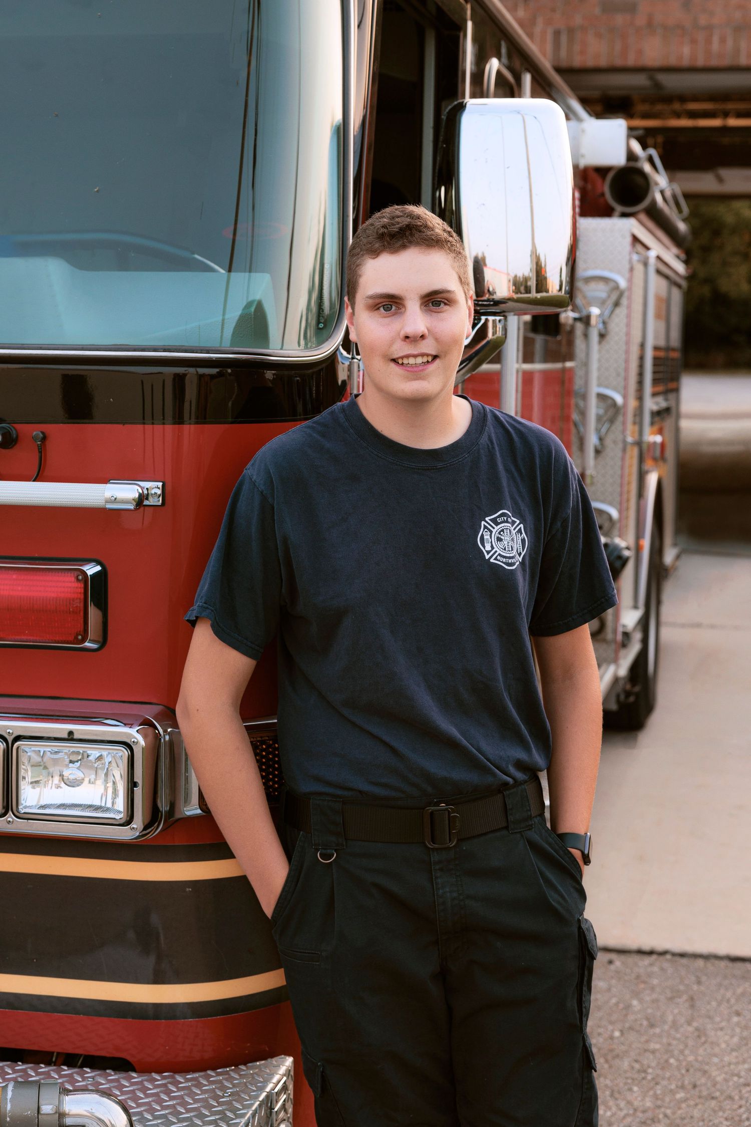 A portrait in front of a red fire truck wearing a navy department t-shirt and dark pants.