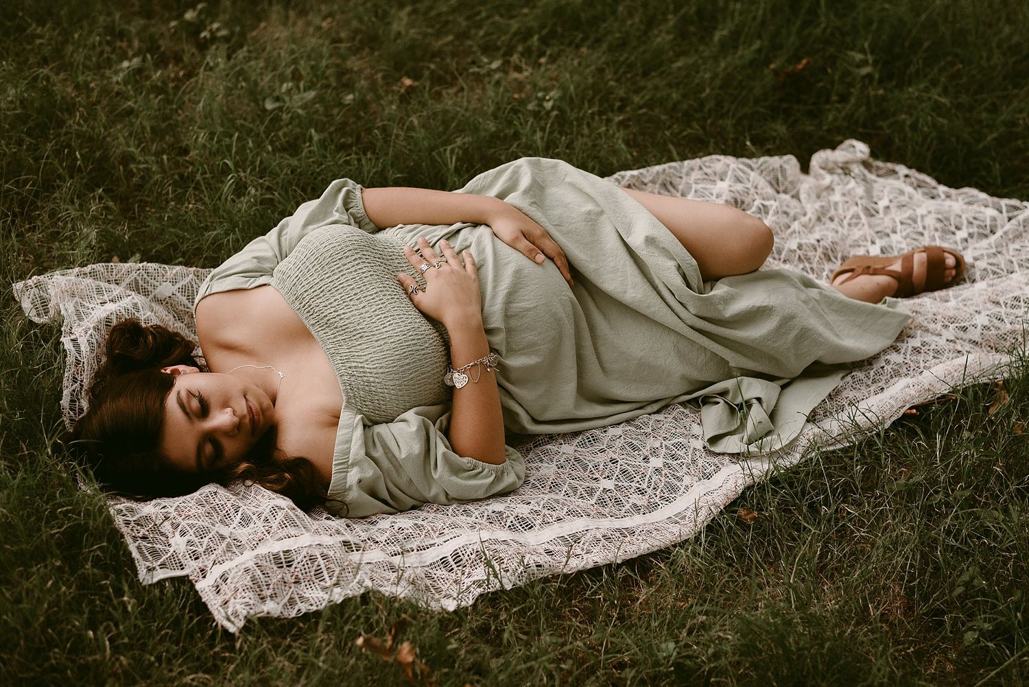 Candid maternity portrait on white lace blanket during golden hour photoshoot.