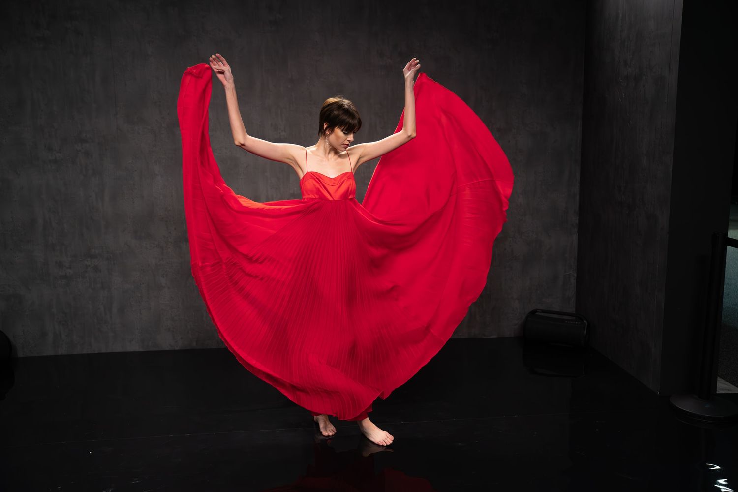 Graceful dance poses in billowing red dress against dramatic black background.
