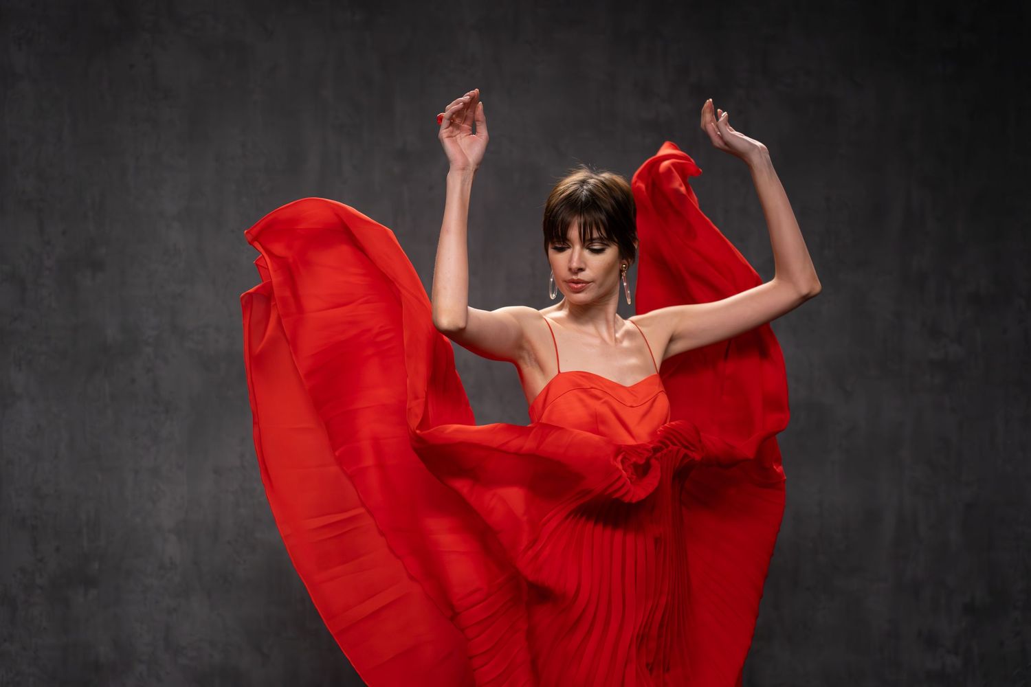 Dynamic movement captured in red dress against moody dark backdrop.