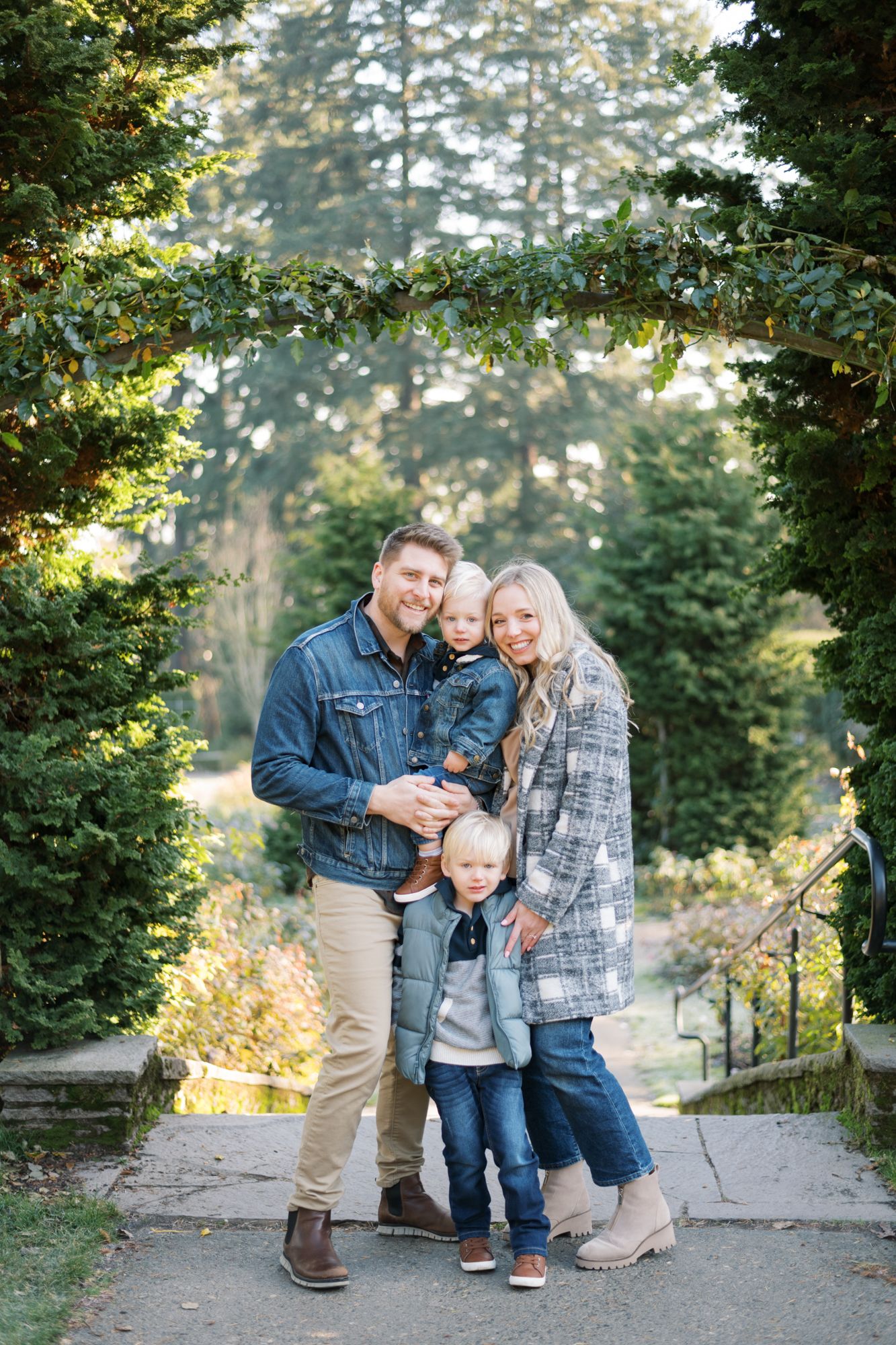 A family portrait on a garden path surrounded by lush evergreen trees.