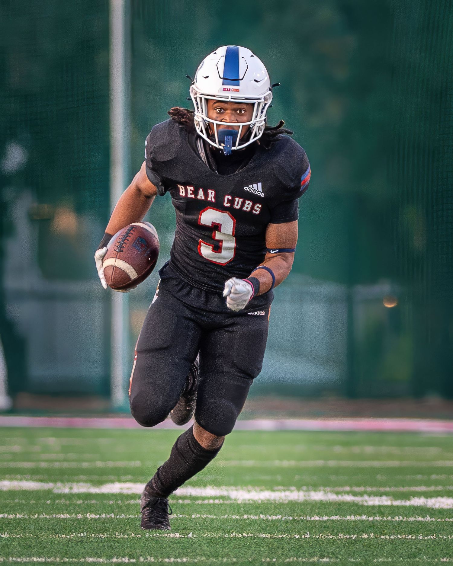 Football player in black uniform runs with ball during competitive game on artificial turf.