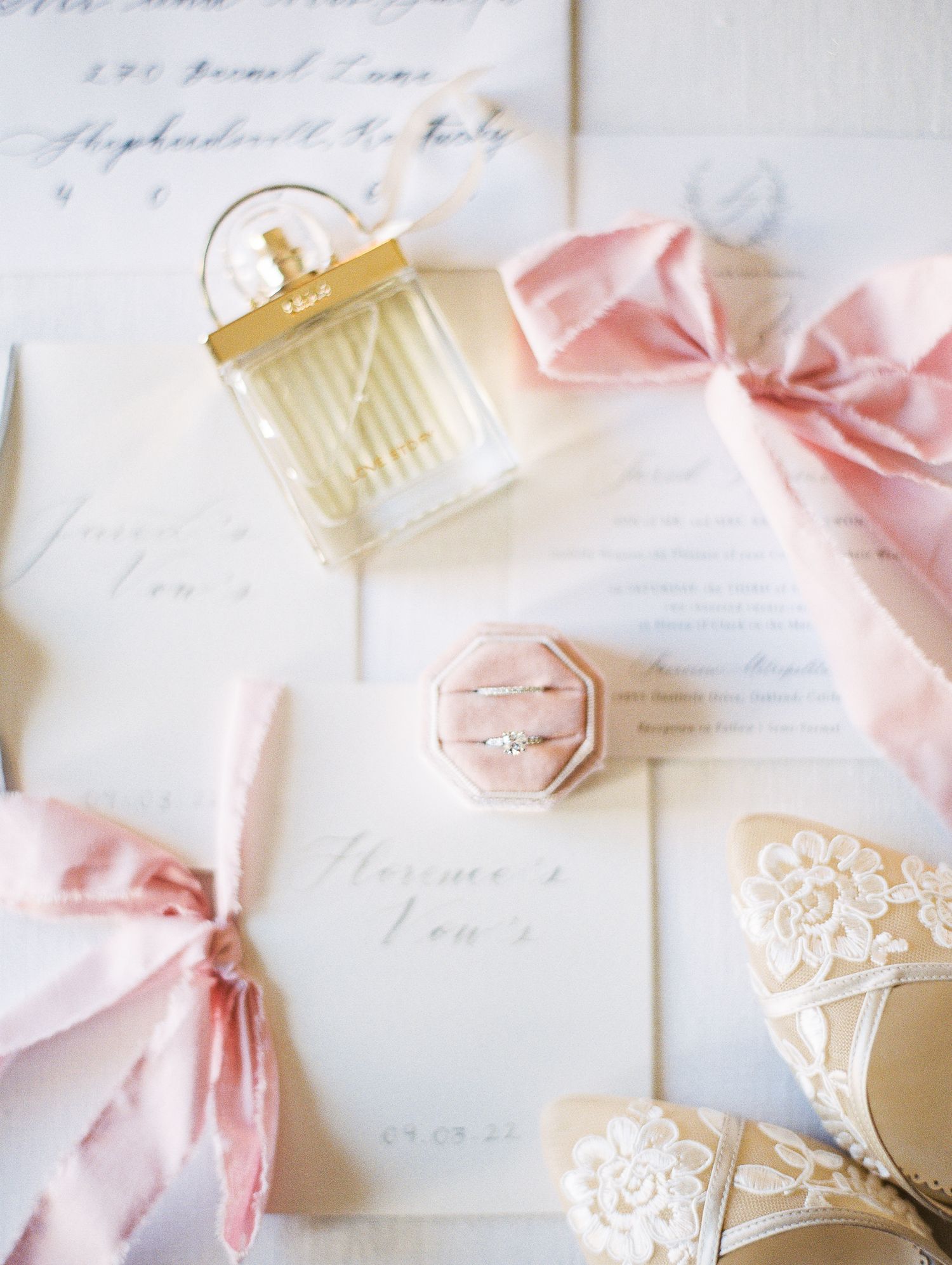 Wedding details featuring a perfume bottle and pink ribbons on elegant stationery.